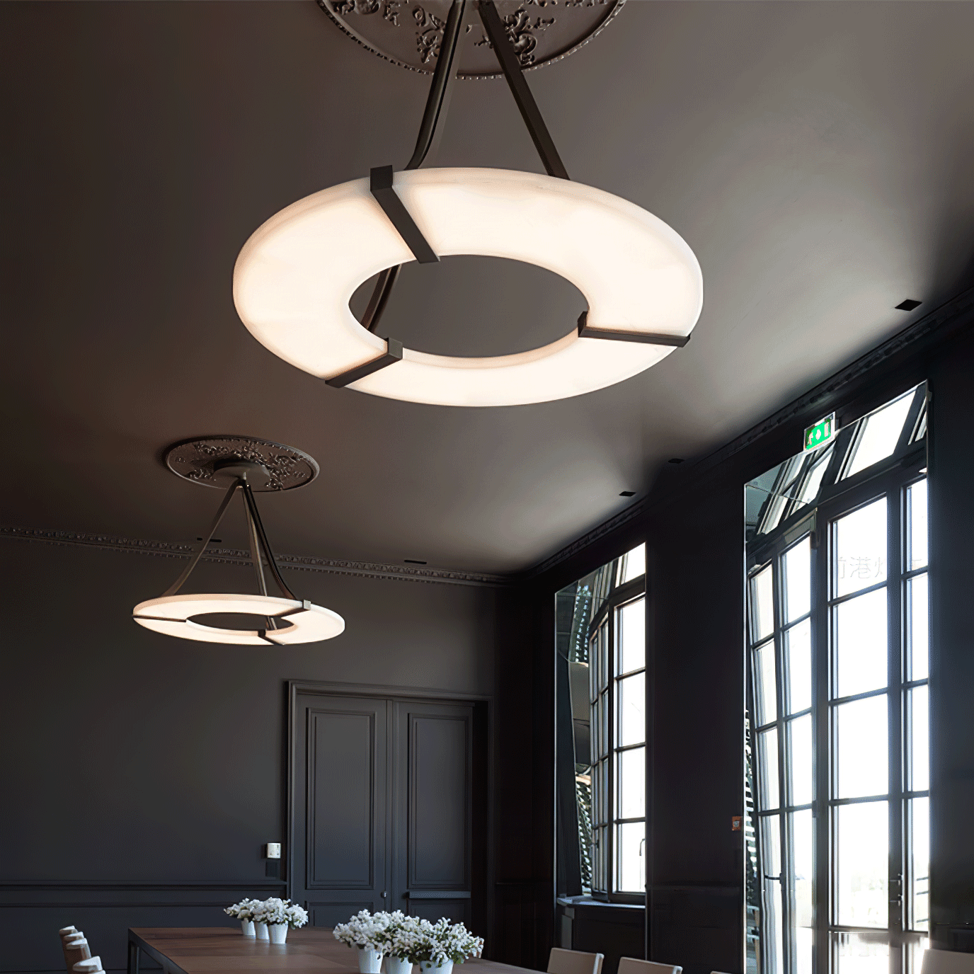Two halo pendants at different distances above wooden table and flowers beside tall dark-framed windows