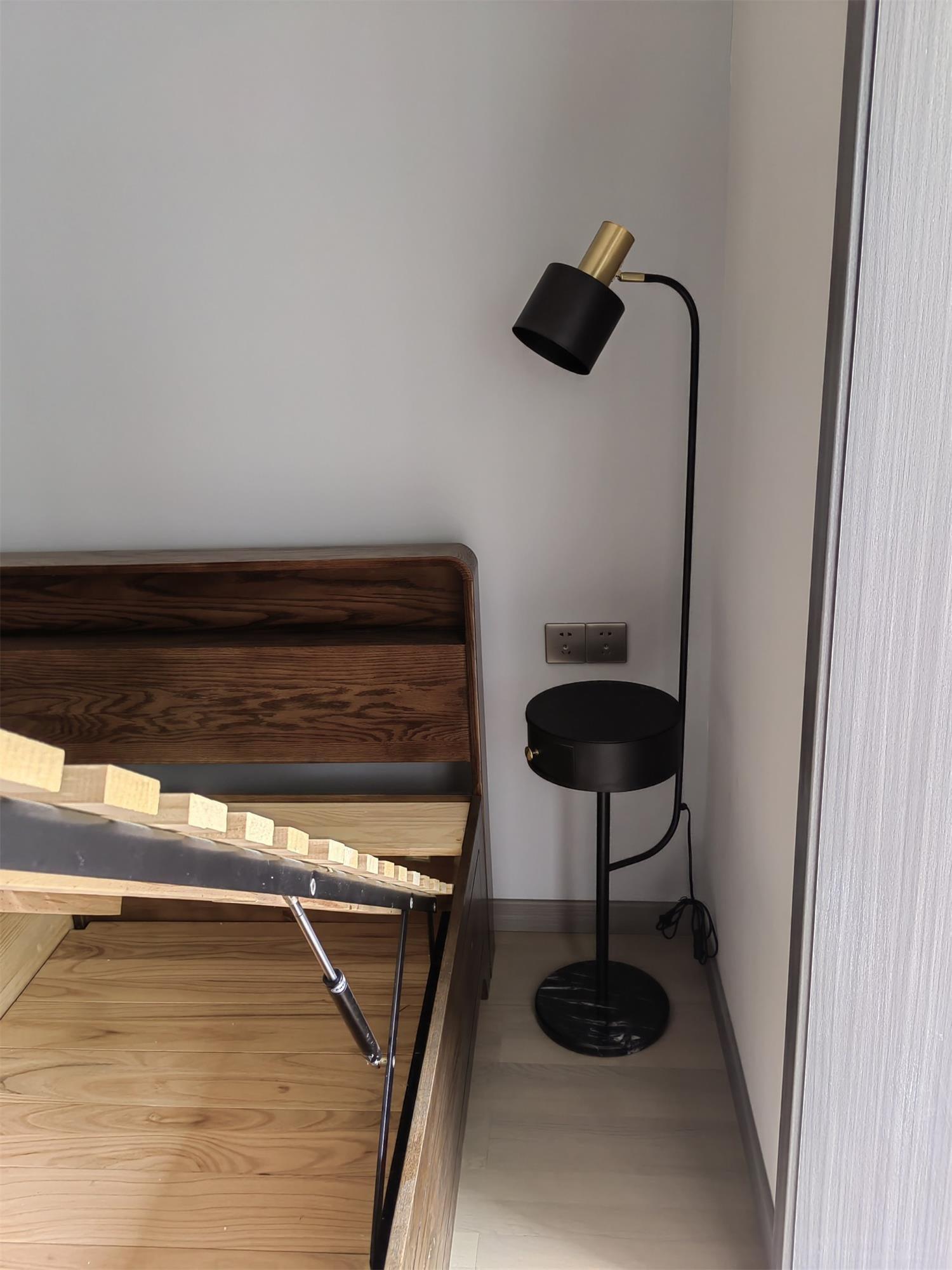 Black Agueda lamp beside wooden bed frame, gold upper fitting, black shade and closed drawer table, dark veined base and cord