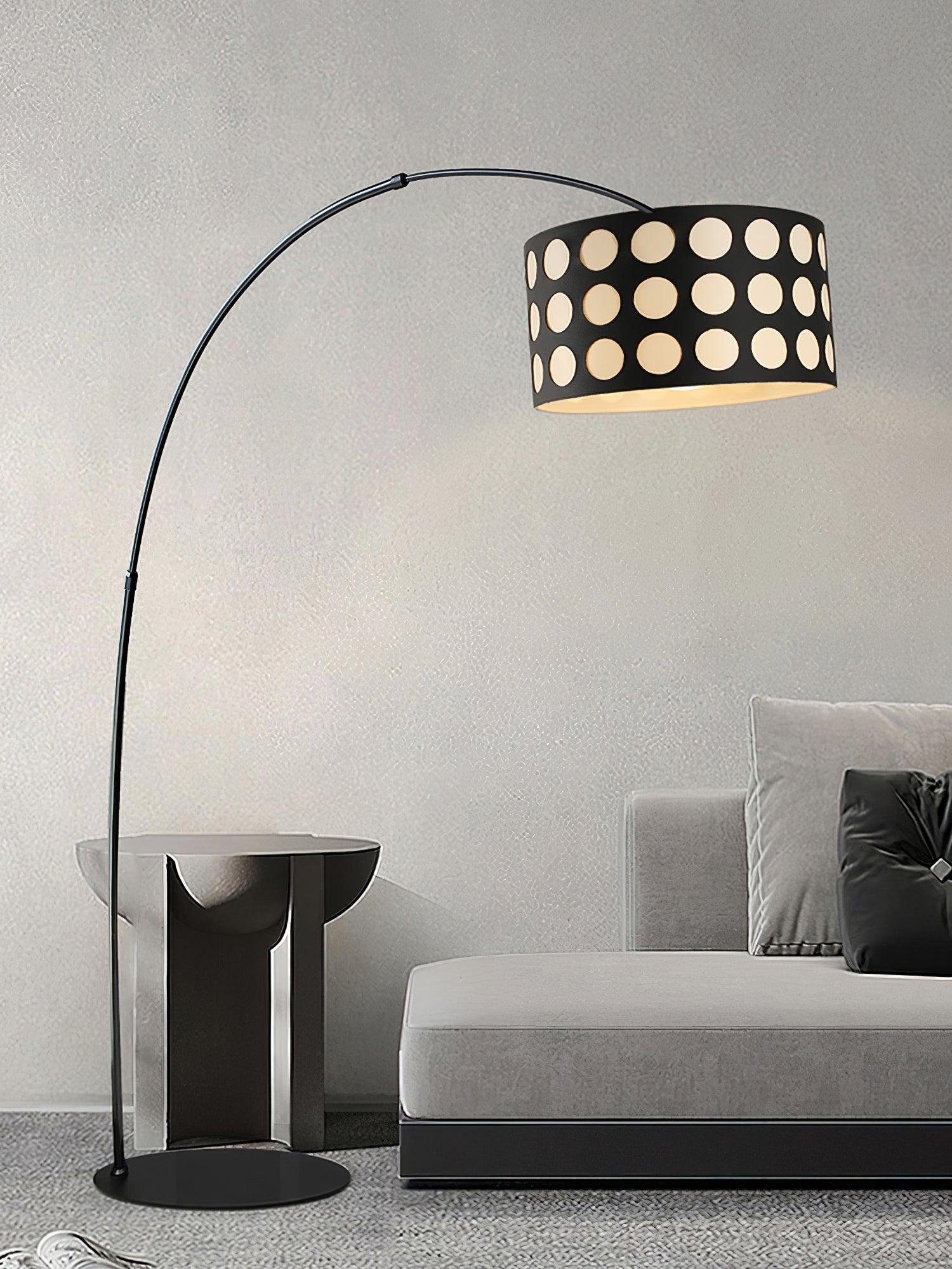 Portrait view of dotted-shade arc lamp beside pale sofa and reflective round side table, circular base on rug
