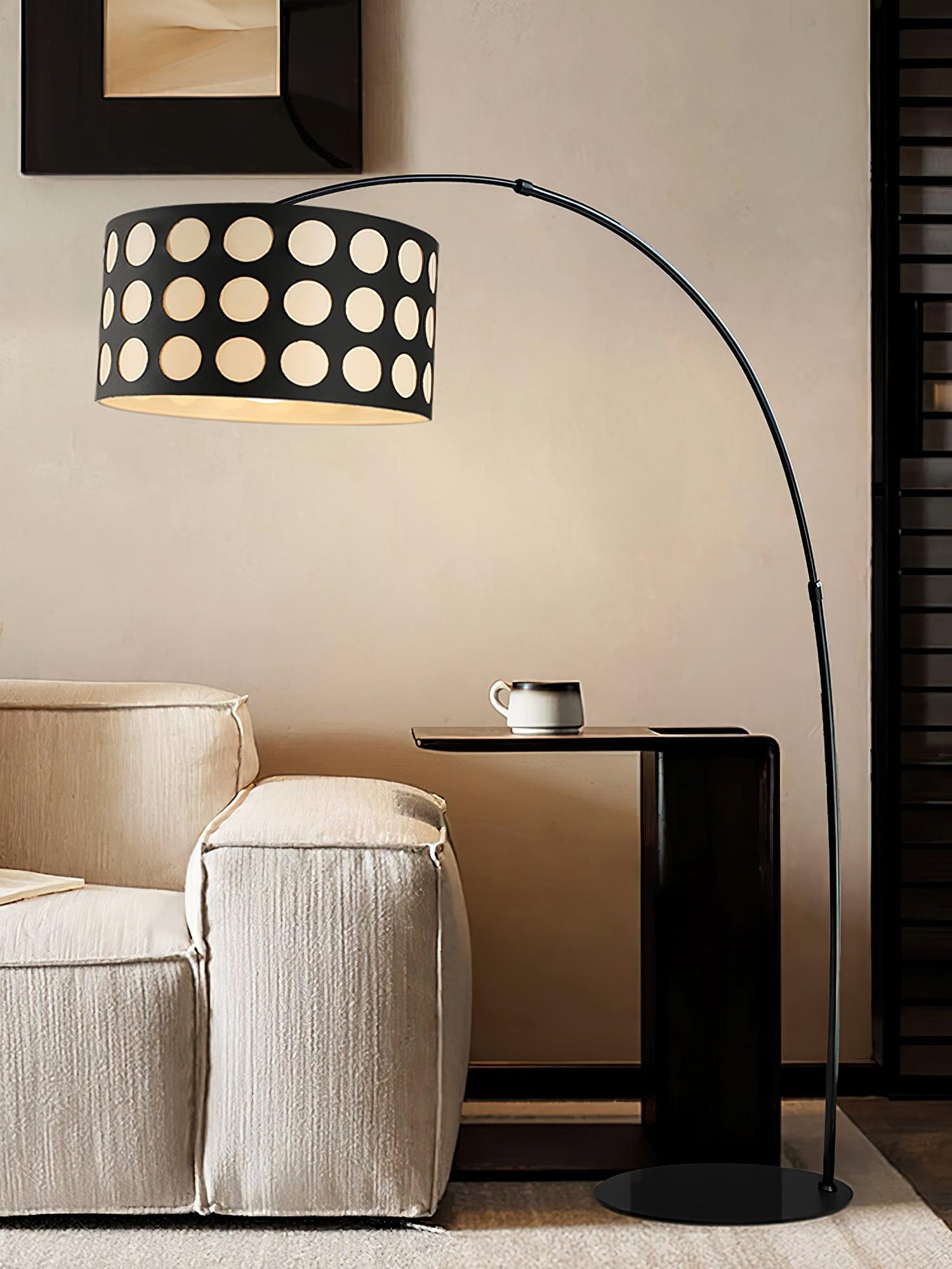 Dotted-shade black arc floor lamp over pale armchair beside dark side table and cup, circular base on rug