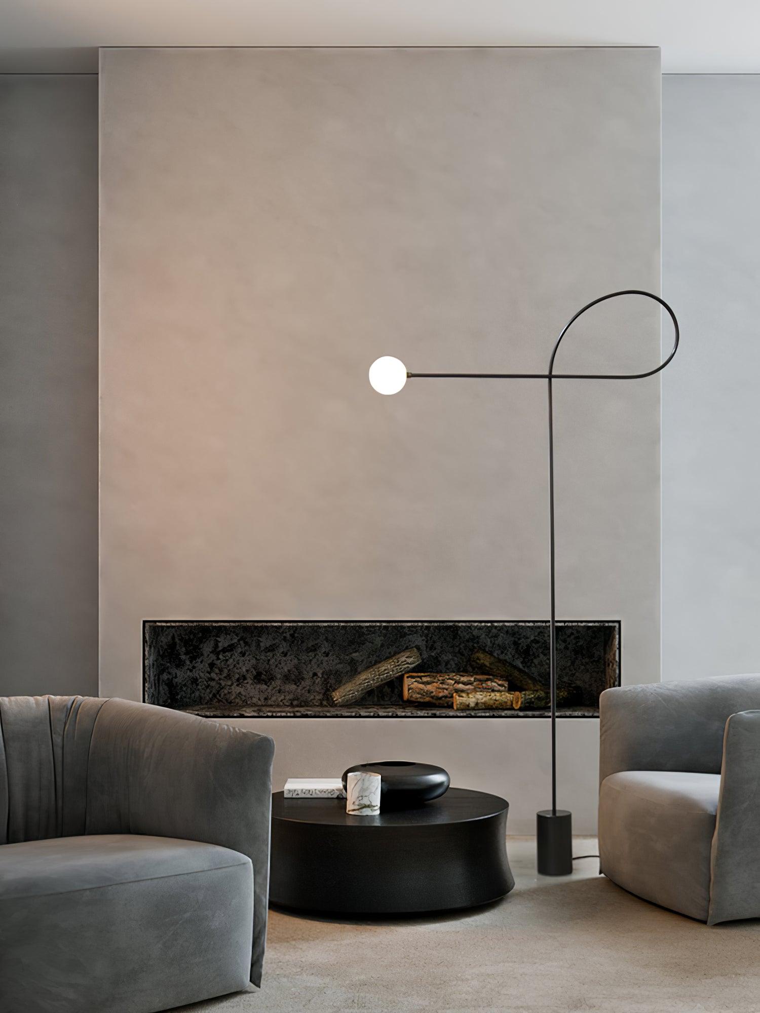Tall lit view of the black loop lamp and white globe beside grey sofas, a black coffee table and fireplace opening
