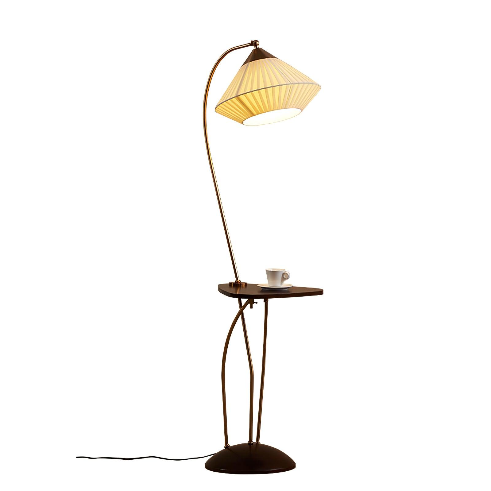 Opposite isolated view of lit Curve with a curved brass-coloured arm, pleated shade, cup-topped table and cable to the left
