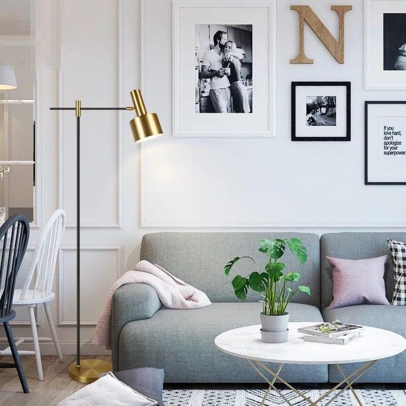 Black and gold floor lamp left of grey sofa with pink throw, white coffee table, plant and wall photographs