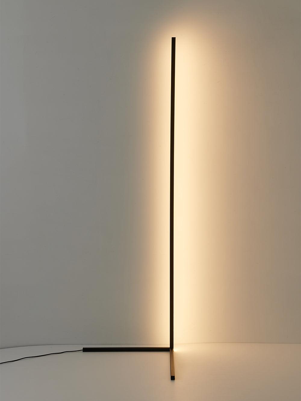 Angled view of a black corner lamp with warm wall glow at the right and power cord extending left