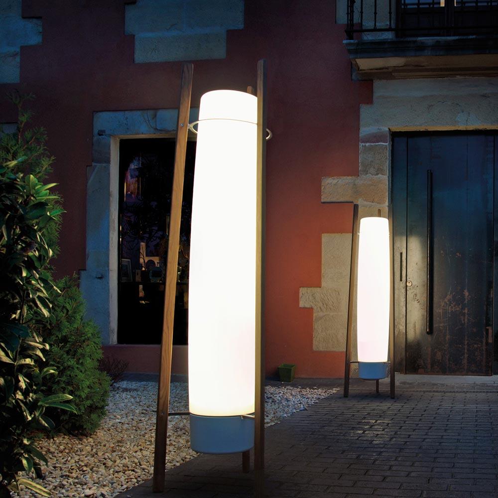 Night view of two glowing column lamps with wooden supports outside a terracotta and stone facade near a wood door