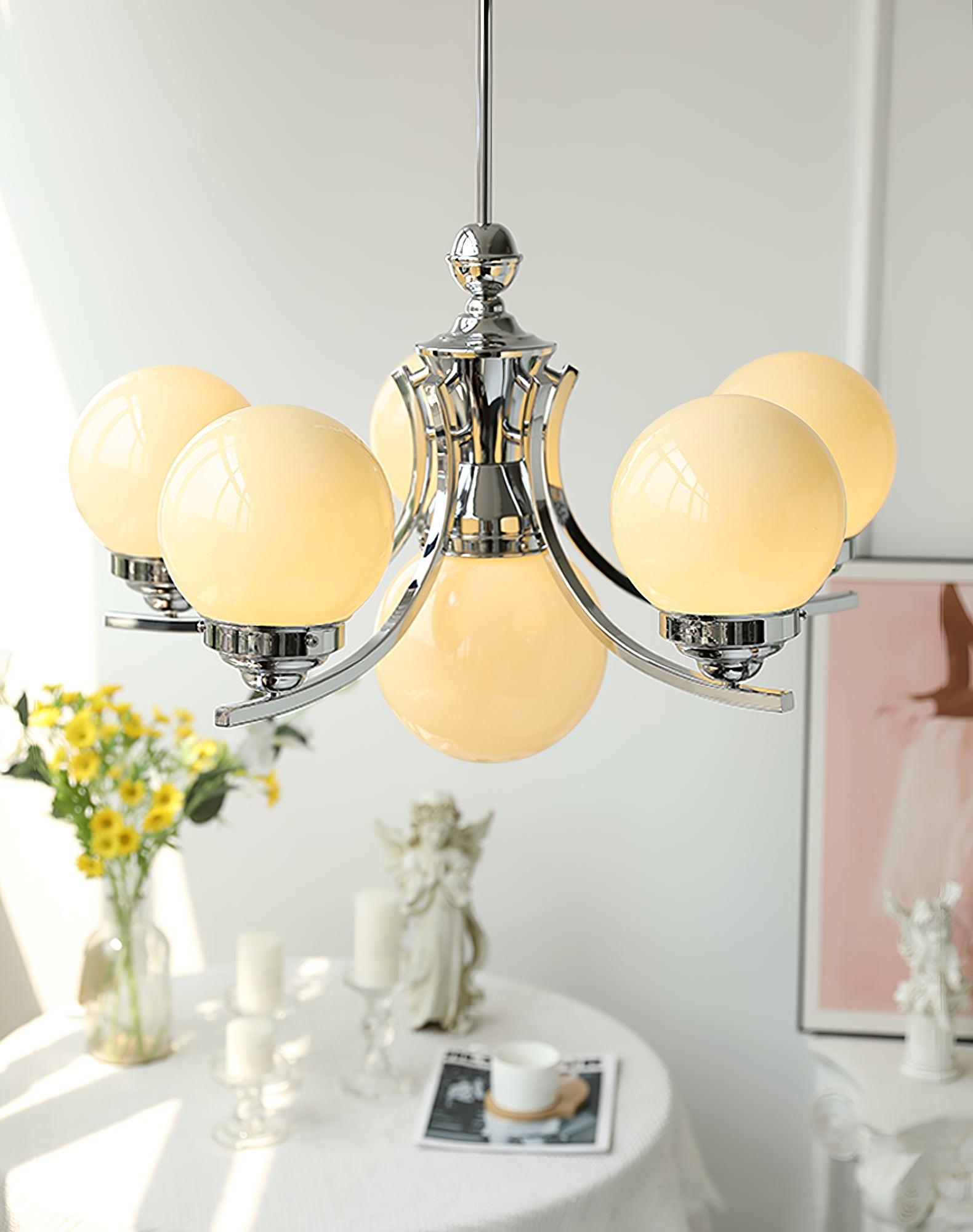 Warm-looking globes on a larger rising-arm chandelier above a white counter with flowers and a cup
