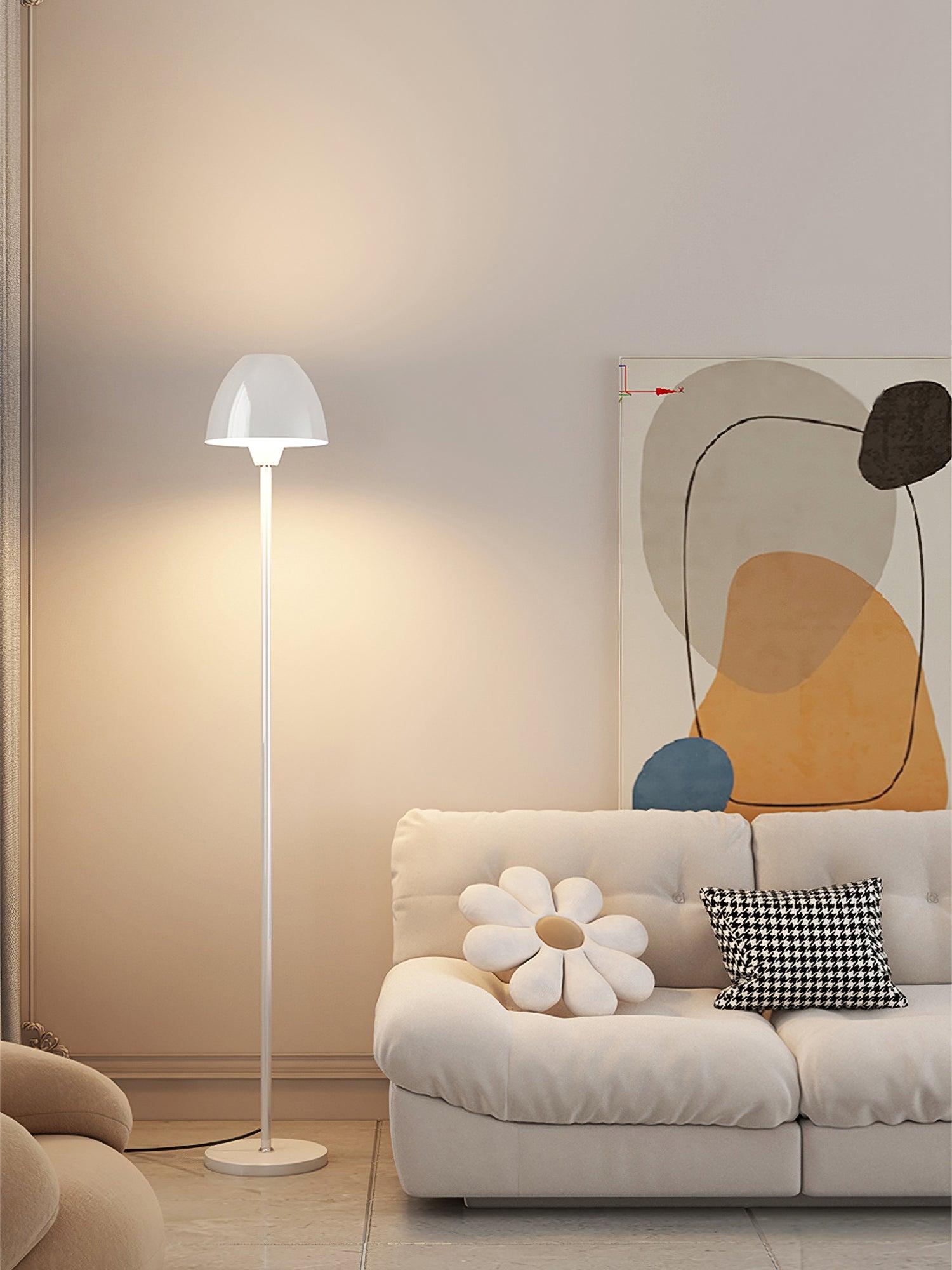 Tall view of a white floor lamp beside a sofa with flower and houndstooth cushions beneath abstract artwork