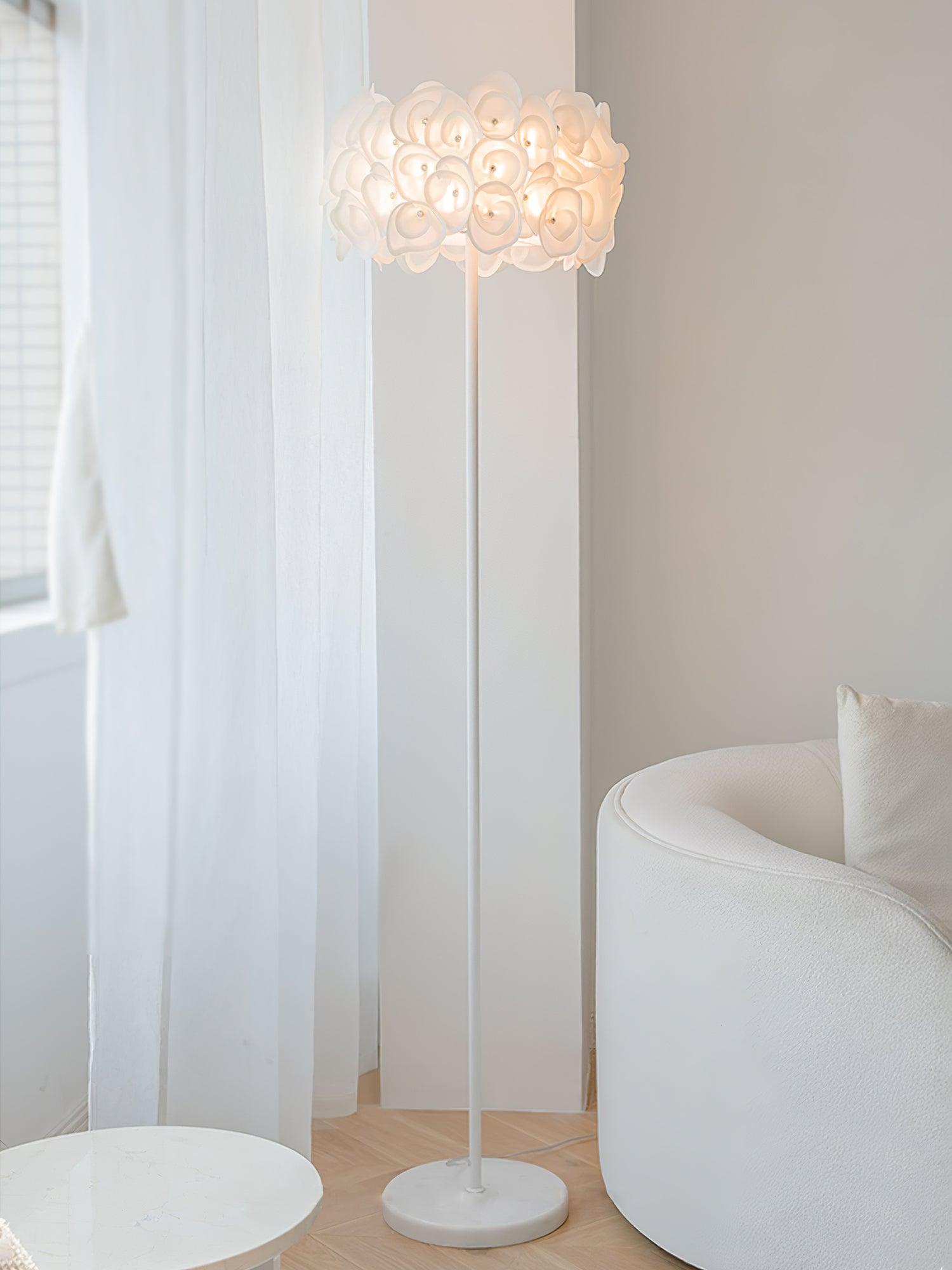Upright white petal lamp by sheer curtain and white barrel chair, slim pole, pale round base and white foreground table