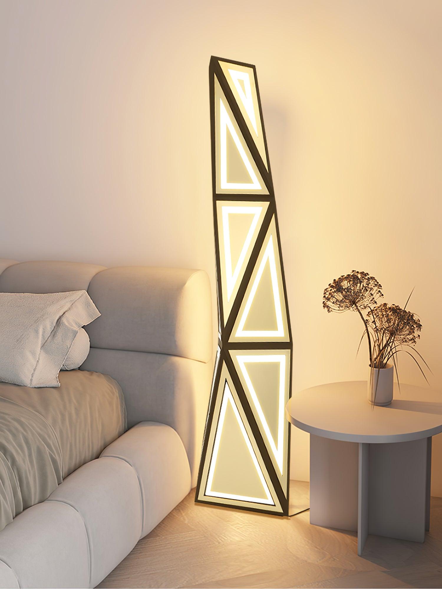 Close room view of lit triangular outlines and gold facets beside a cream sofa and round side table