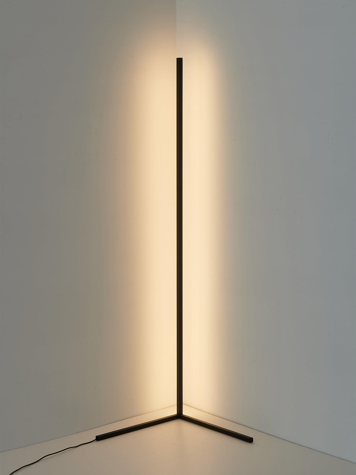 Complete black lamp casting warm corner light, with two angled feet and cord exiting to the left