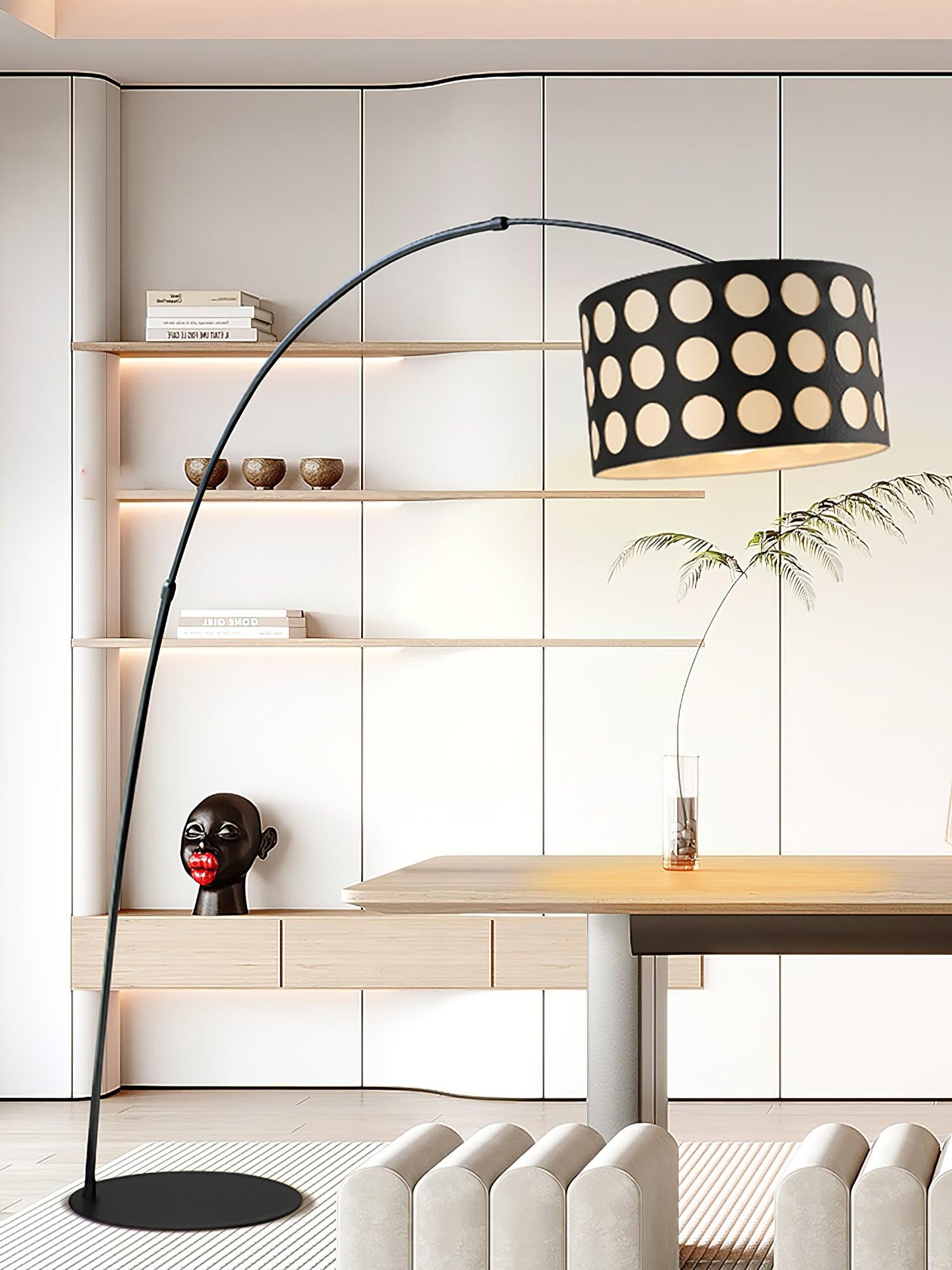 Portrait black arc floor lamp with dotted shade above desk area, pale sculptural bench and wall shelving
