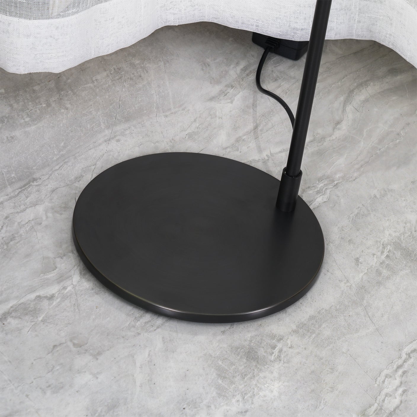 Close-up of black round lamp base and lower stem with cable and black box under the curtain