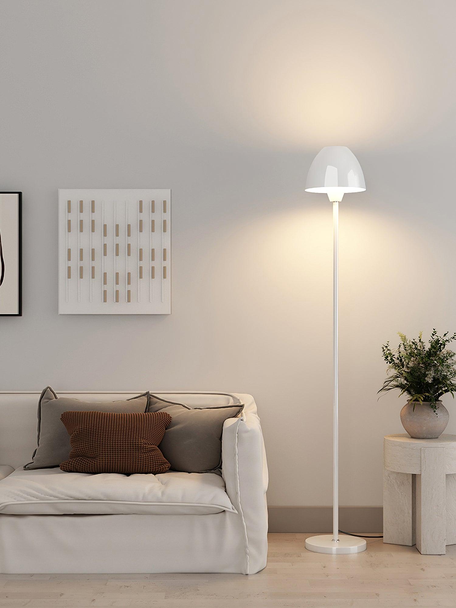 White floor lamp between a pale sofa and a stone-look side table topped with a vase of foliage