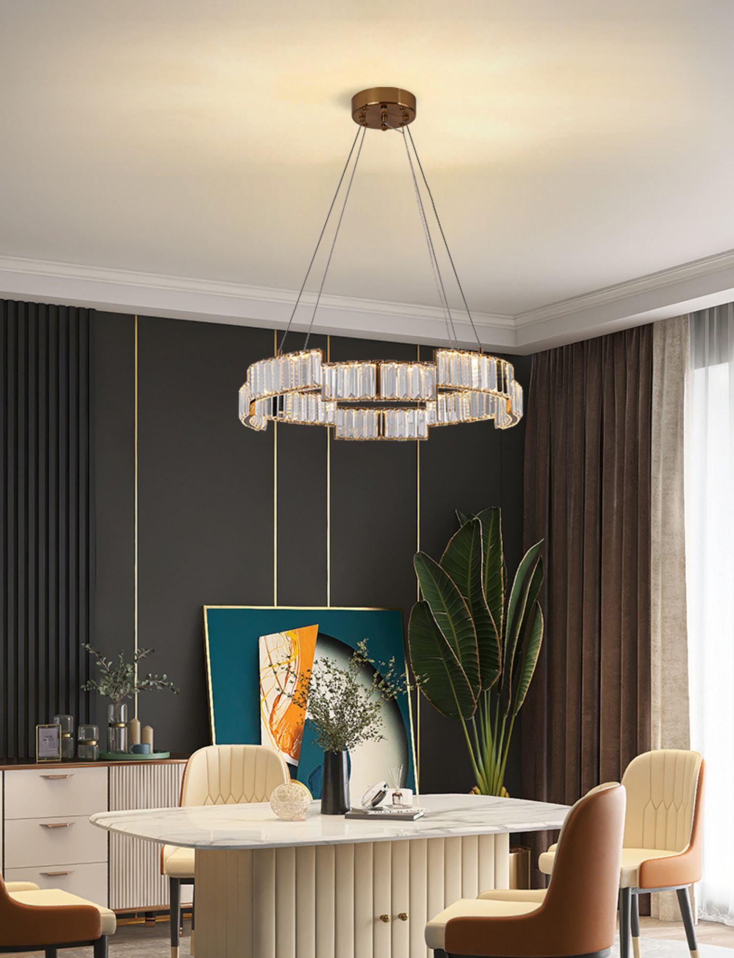 Ring chandelier above an oval marble-pattern dining table with ribbed base, brown and cream chairs, teal art and plant