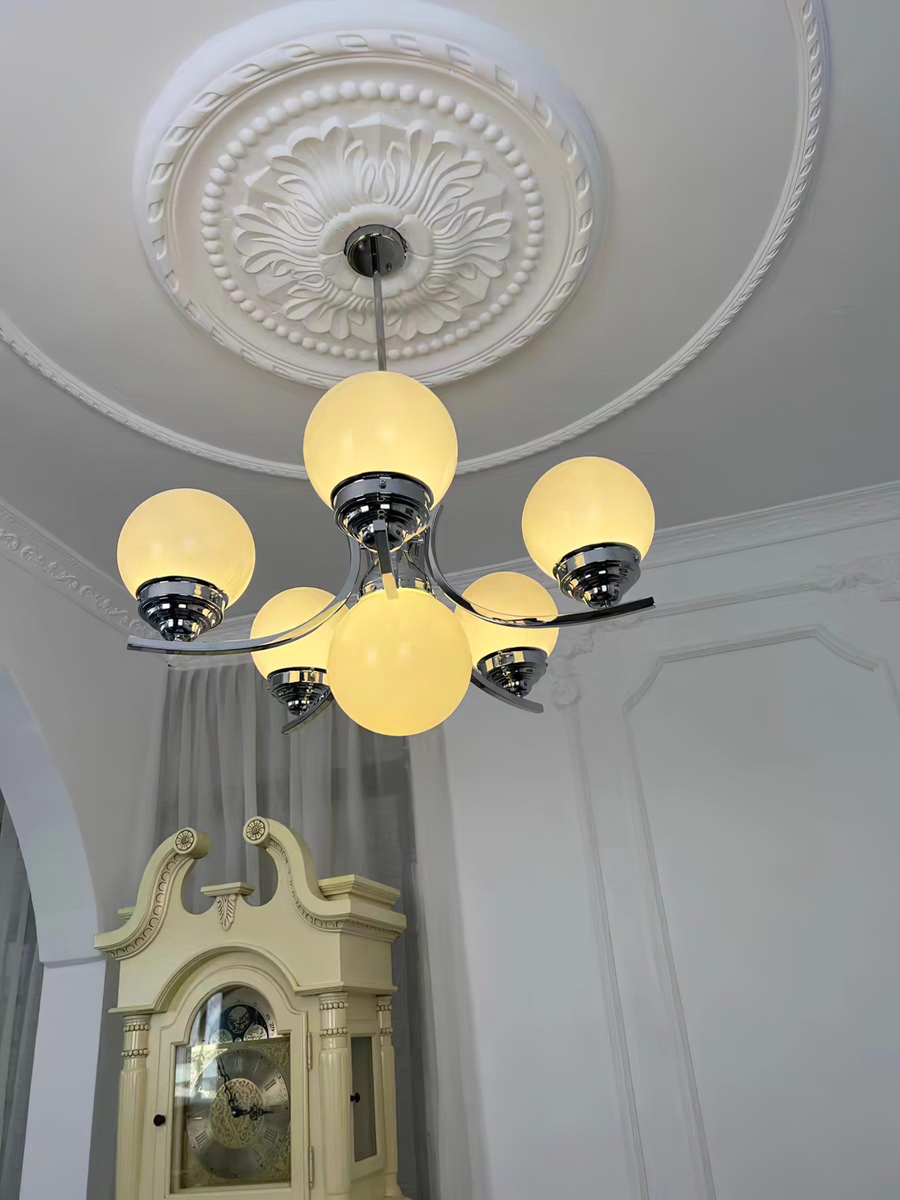 Low-angle view of illuminated Dewdrop globes and chrome arms beneath an ornate white ceiling medallion
