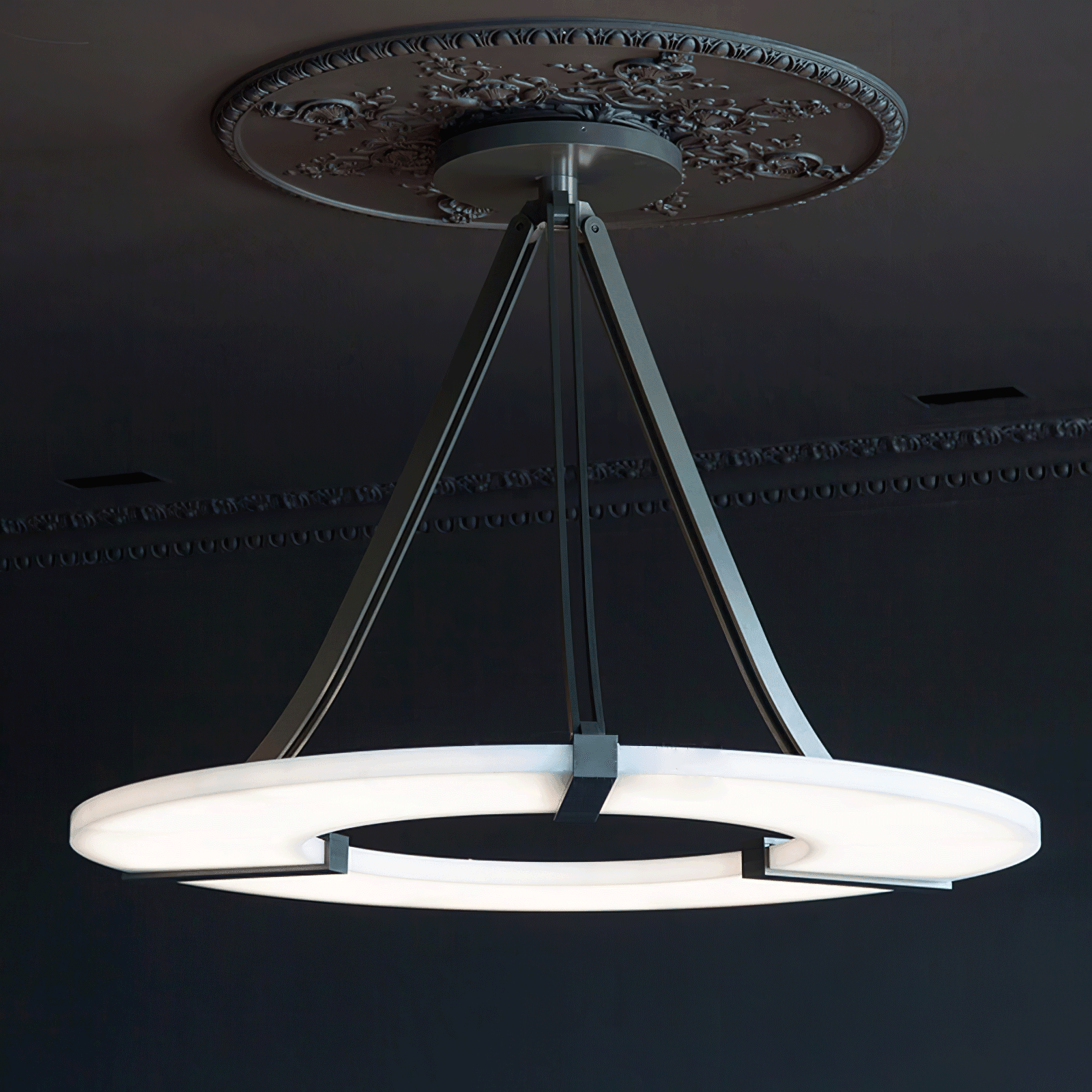 Wide low view of glowing halo pendant and black canopy beneath floral medallion and cornice