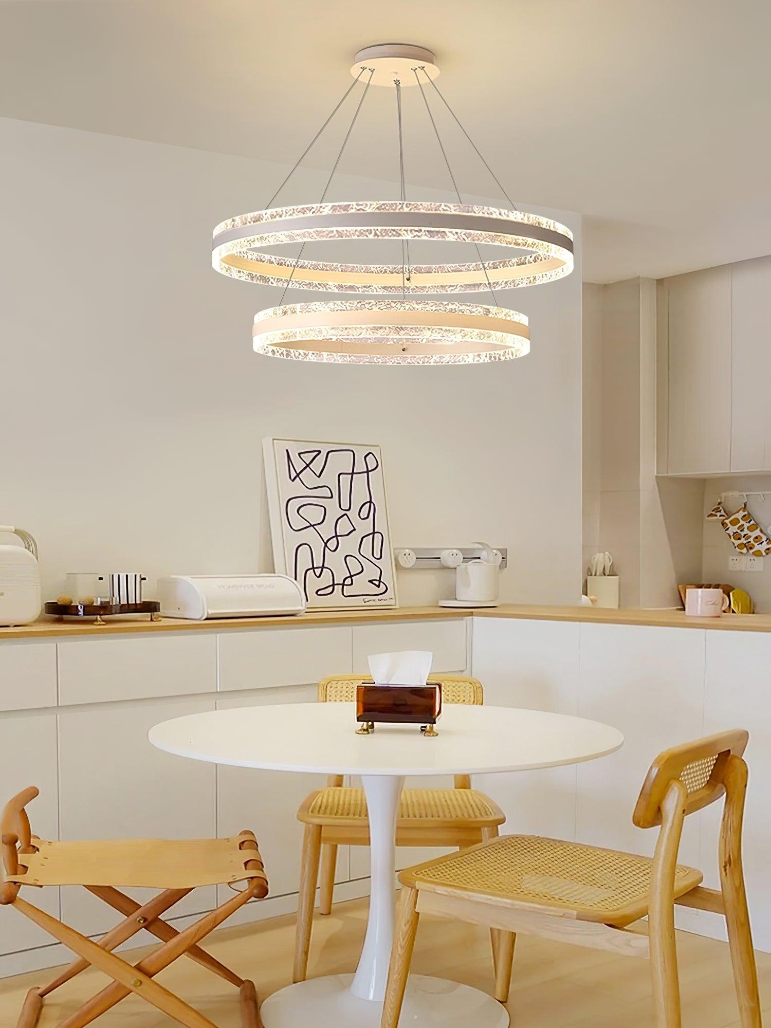 Two glowing rings above a white round dining table with cane chairs and white kitchen cabinets