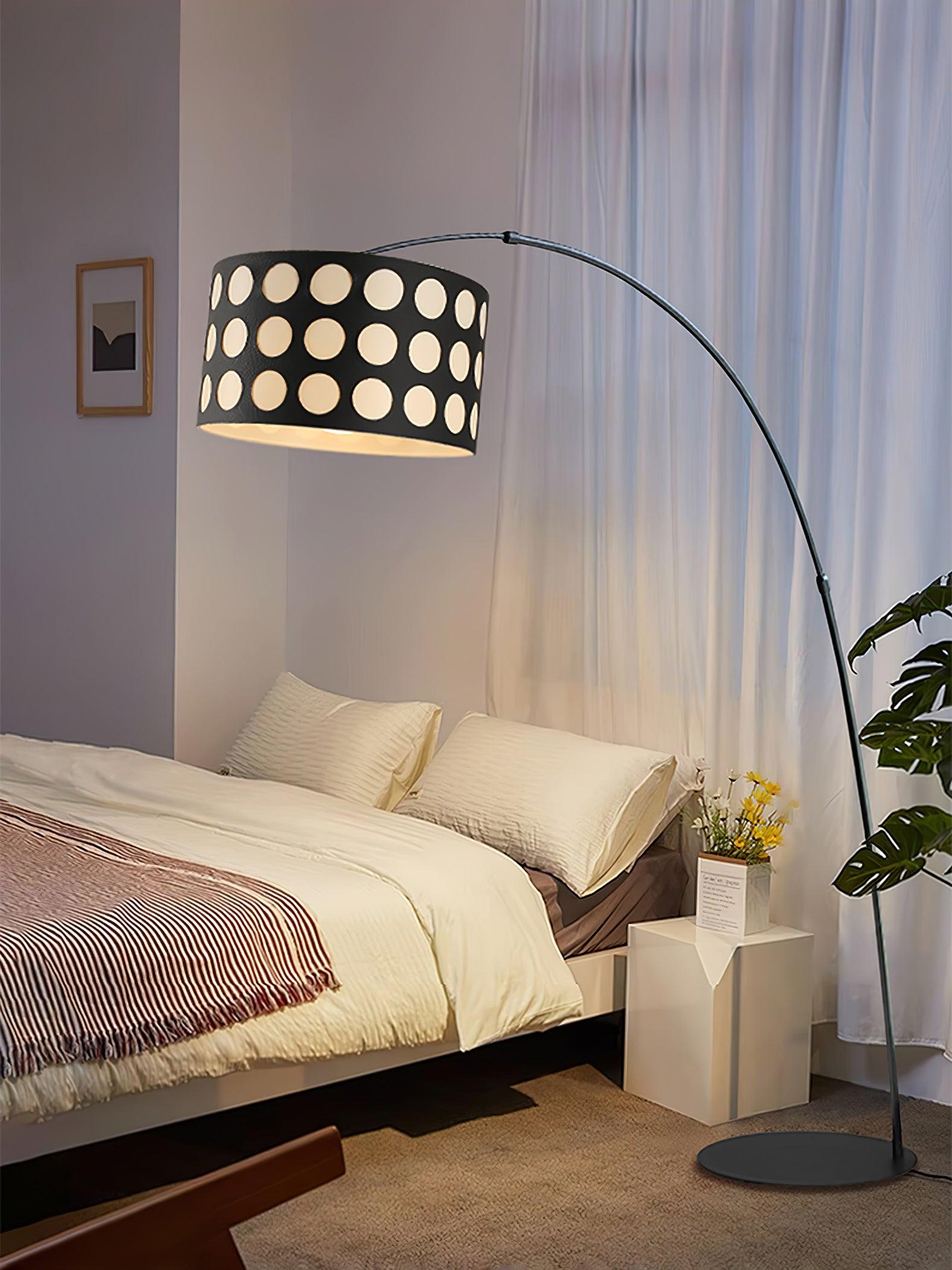 Dotted-shade black arc floor lamp over bedside area, with white cabinet, plant, circular base and trailing cord