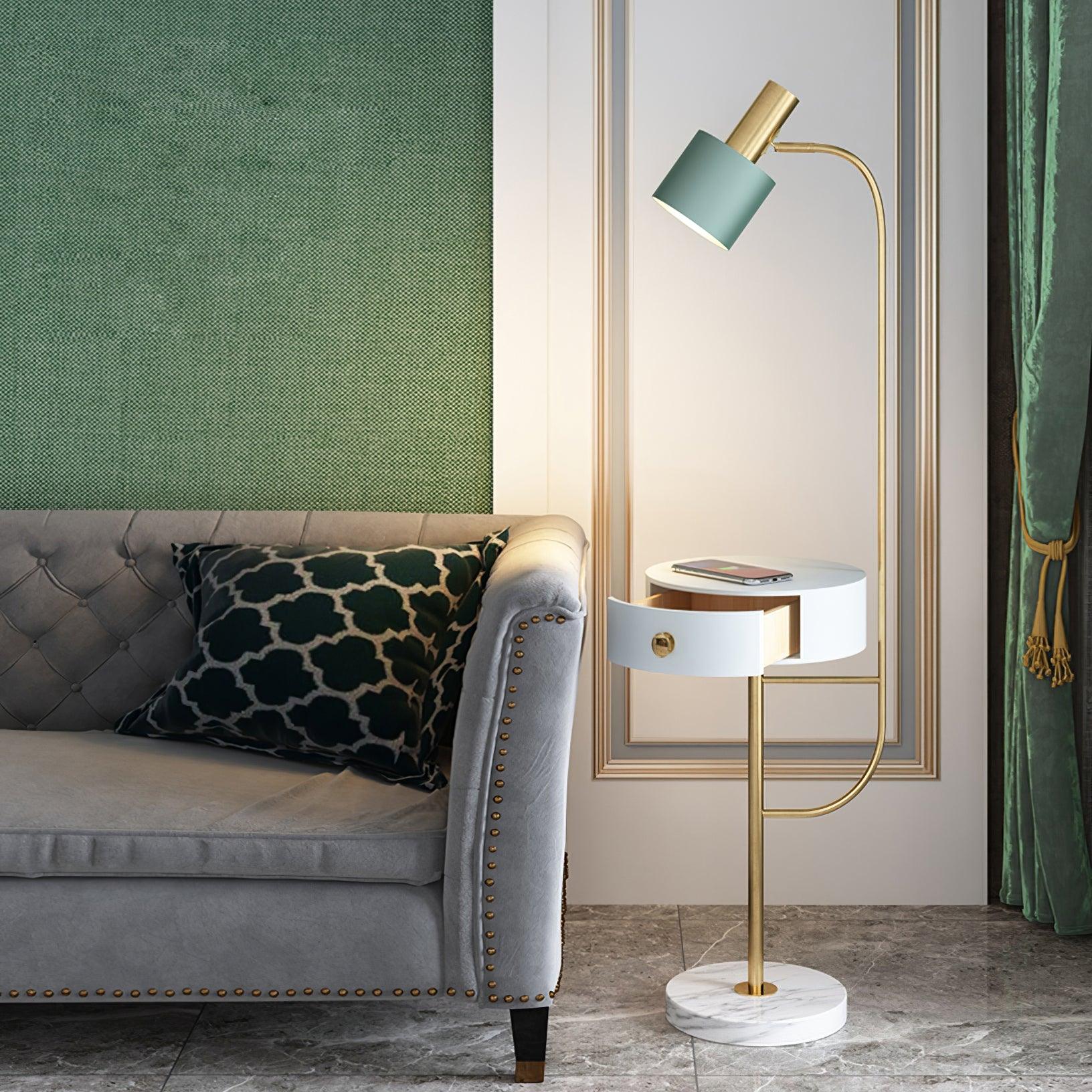 Gold Agueda lamp beside tufted gray sofa, green shade over white round open drawer, phone on table and white veined base