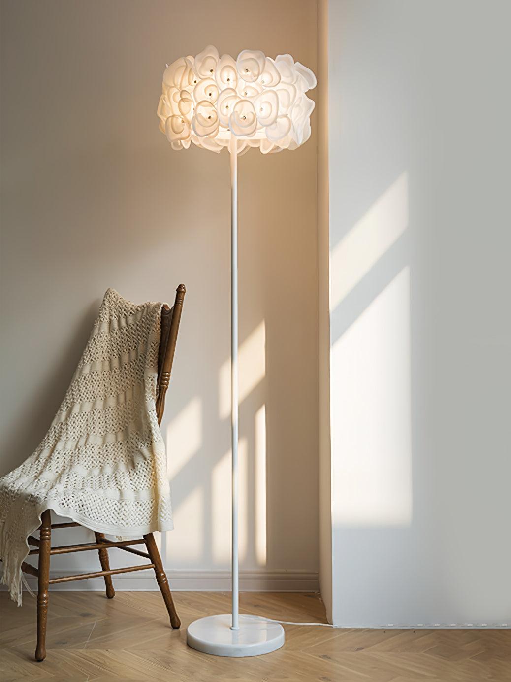 Upright petal lamp lit beside wooden chair with knitted blanket, sunlit wall, white round base and floor cord
