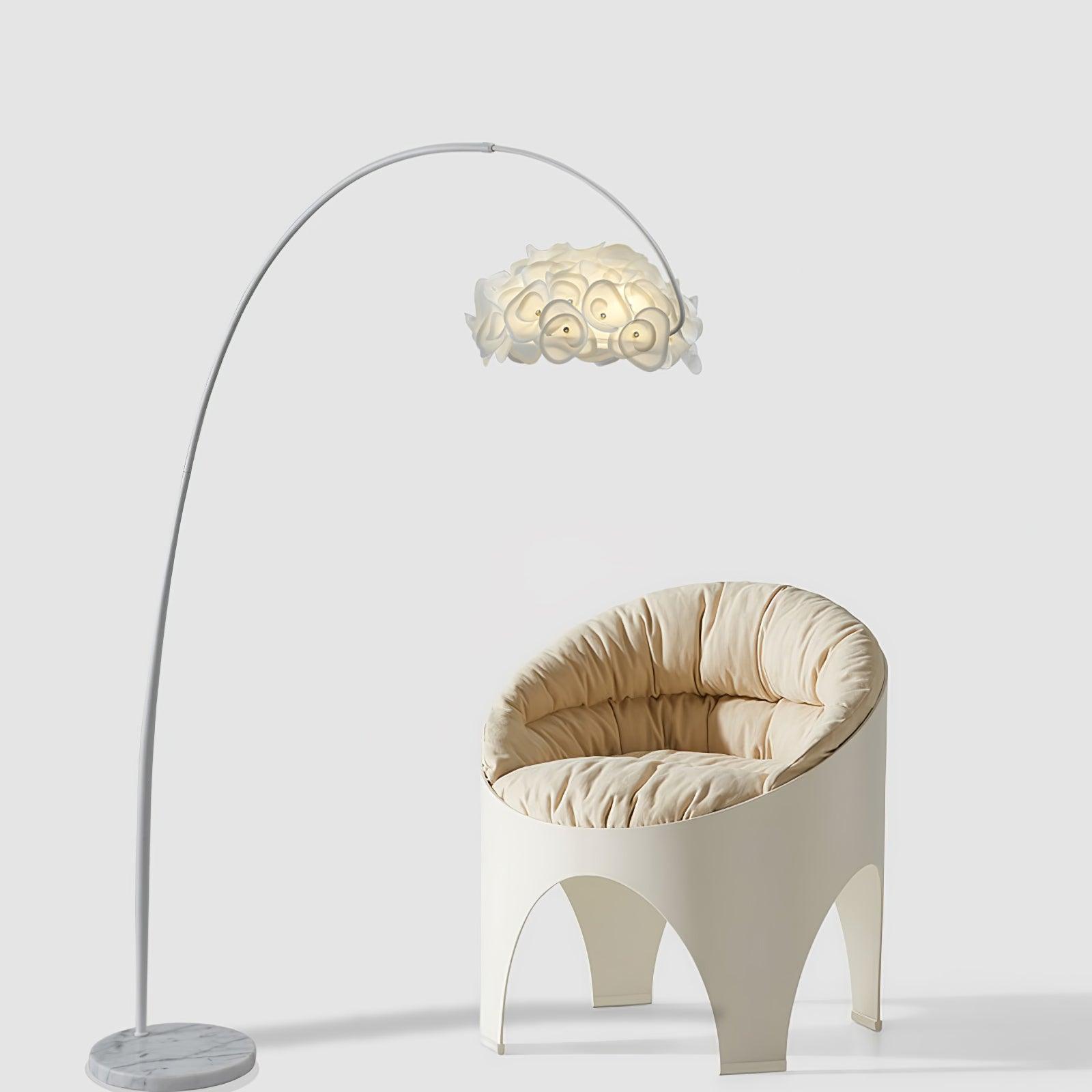 Arched white Hydrangea lamp over cream sculptural chair on plain background, lit petal shade and veined round base