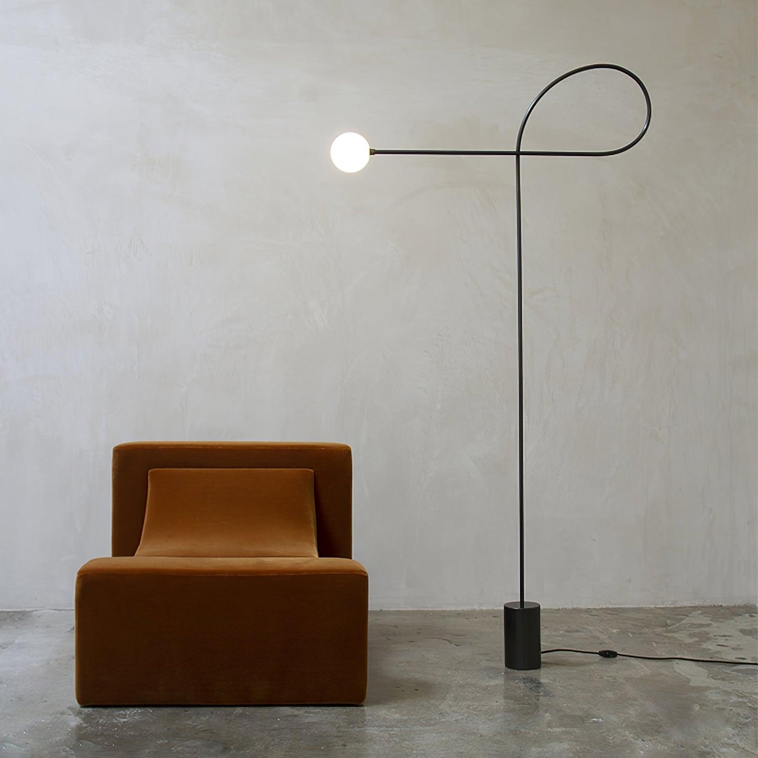 Lit Arcane Orb with a black loop frame and white globe beside an ochre velvet armchair on a concrete floor