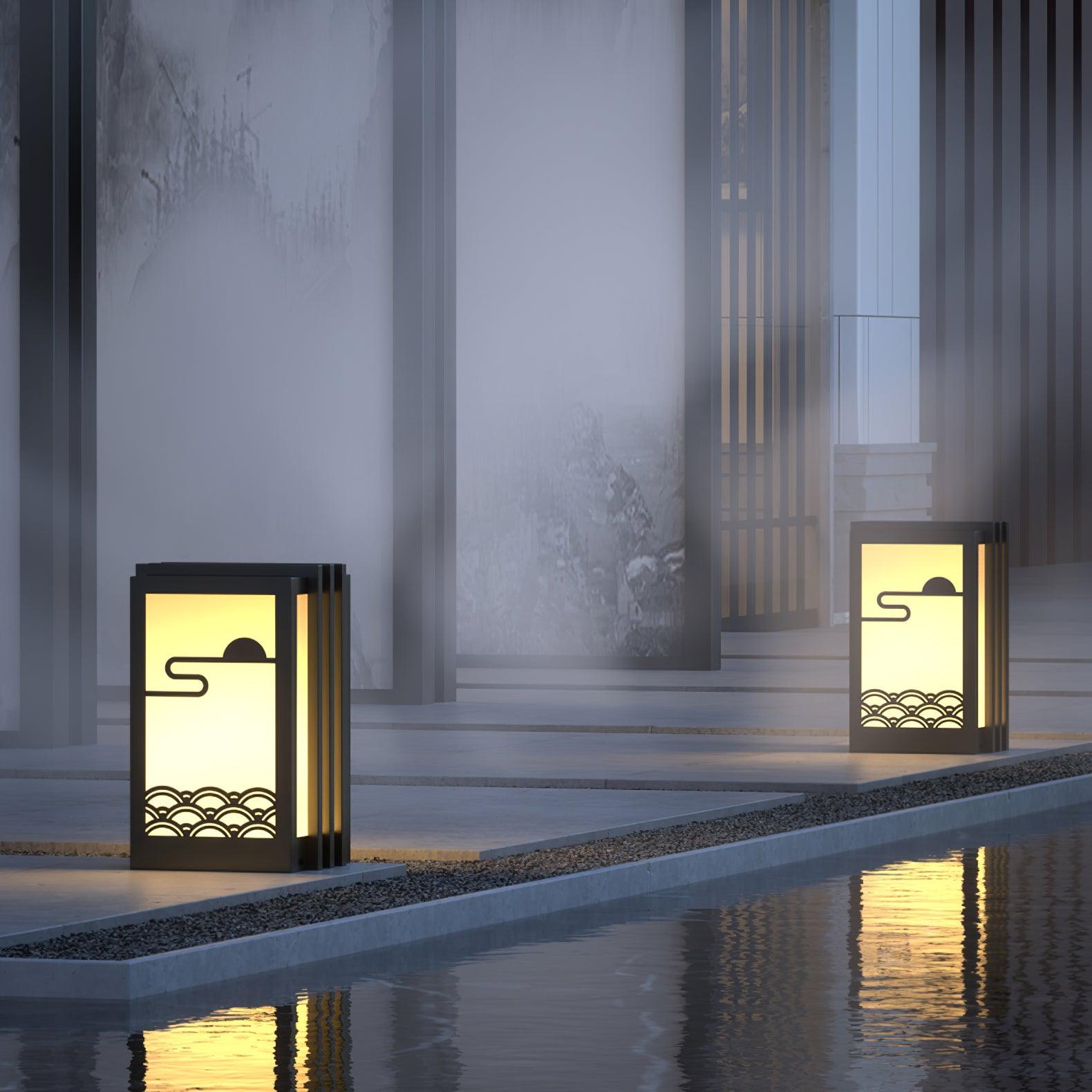 Two lit sun-and-wave lanterns beside water channel, with reflections, gravel strip and pale garden wall