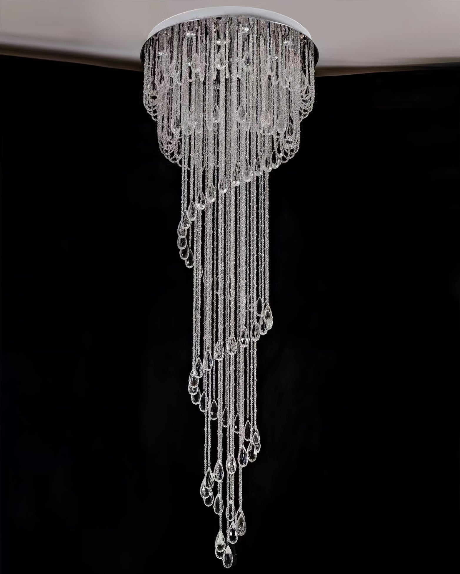 Unlit clear crystal spiral against a dark wall, showing a round silver canopy and scalloped upper bead rows
