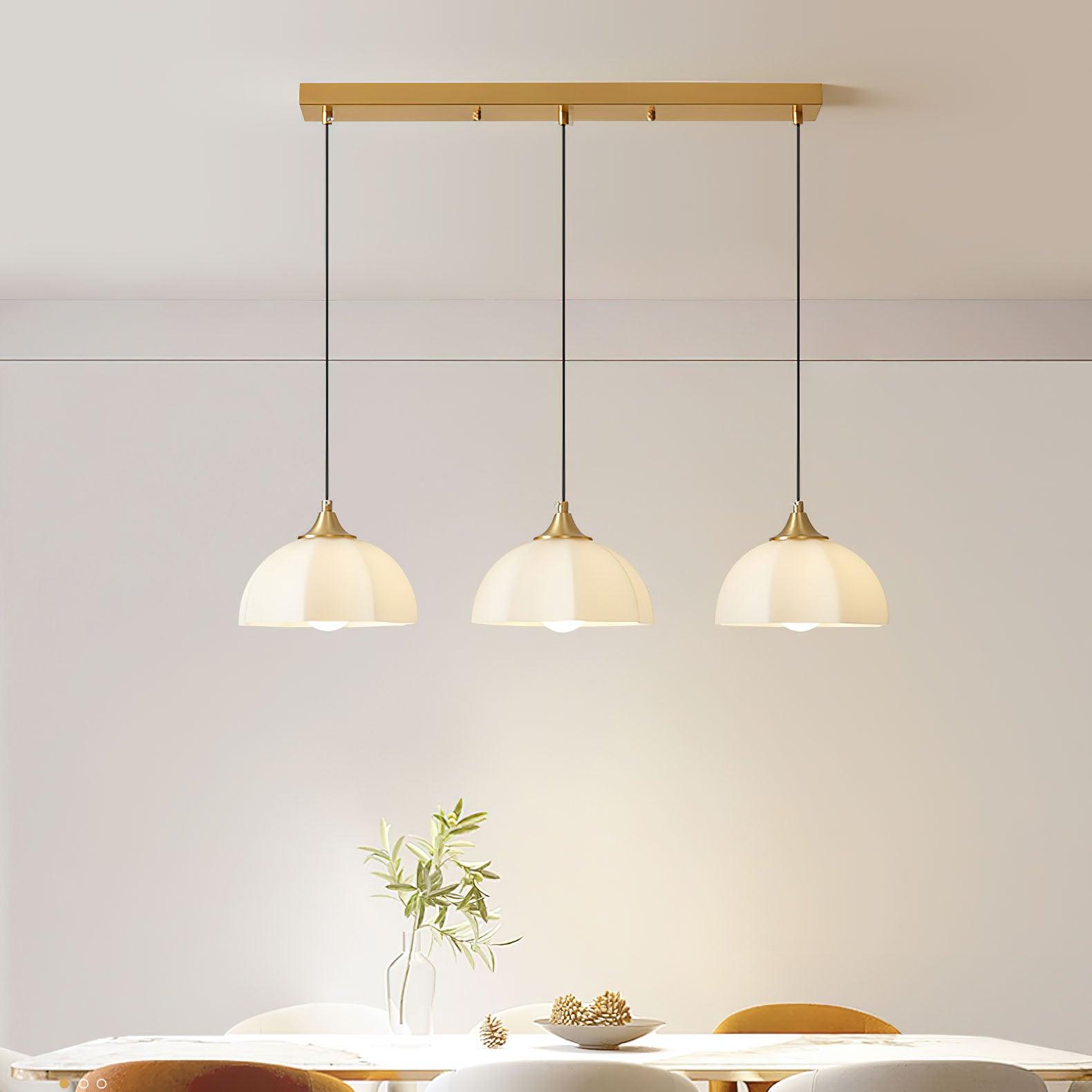 Linear three-shade brass pendant over a table