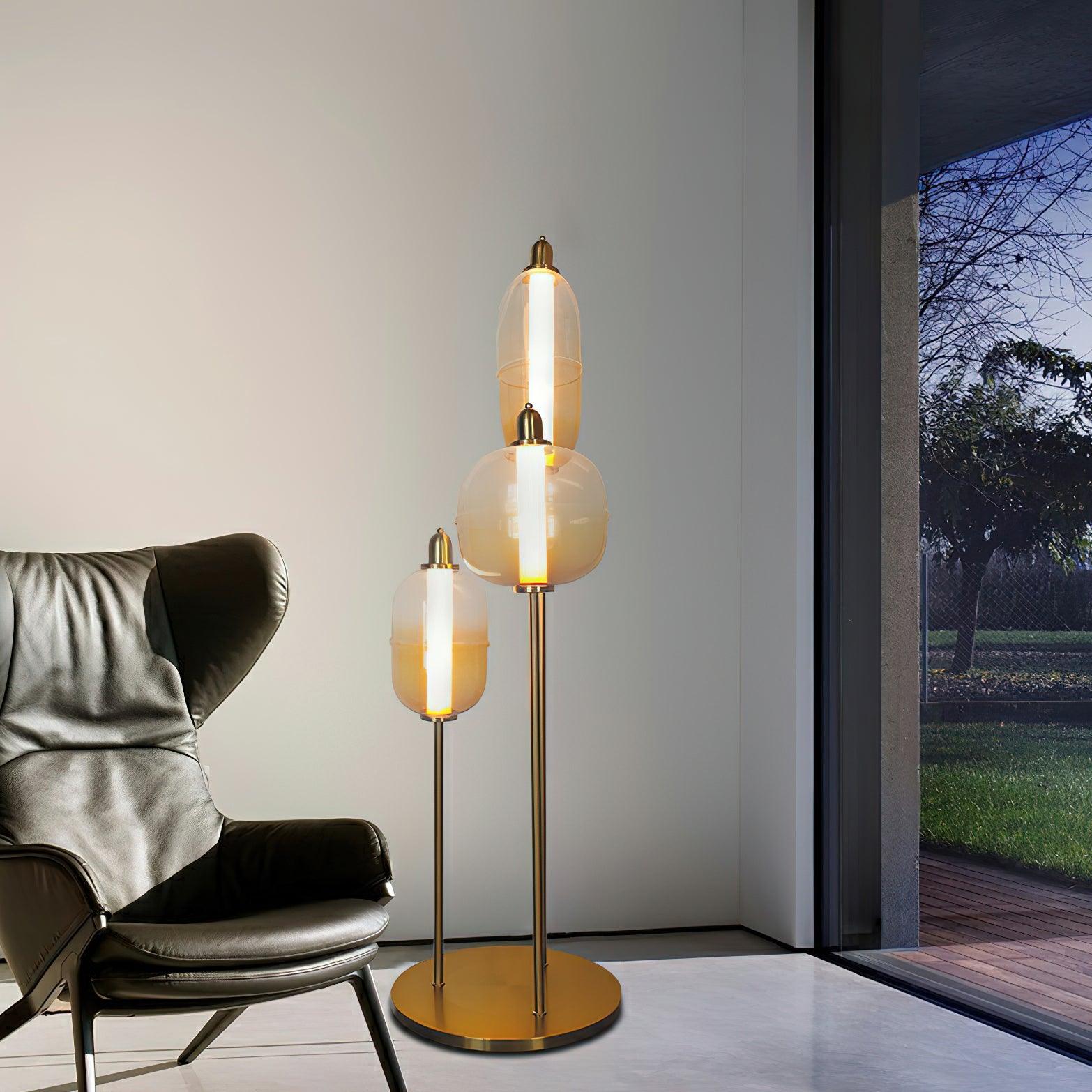 Illuminated amber glass shades on a gold floor stand beside a dark leather chair and a window overlooking a patio