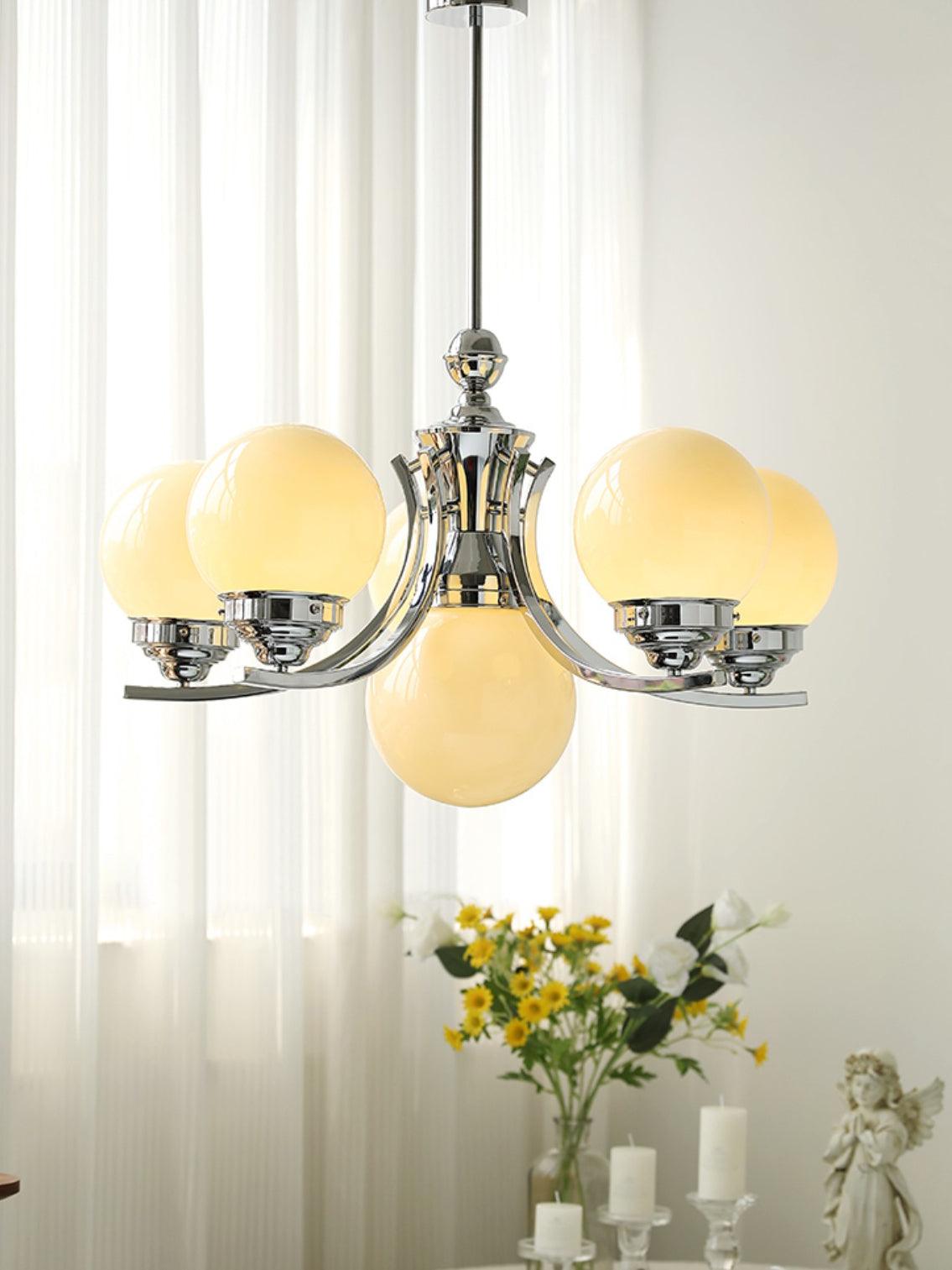Rising-arm chrome globe chandelier above flowers and candles by white curtains, with rod and round canopy visible