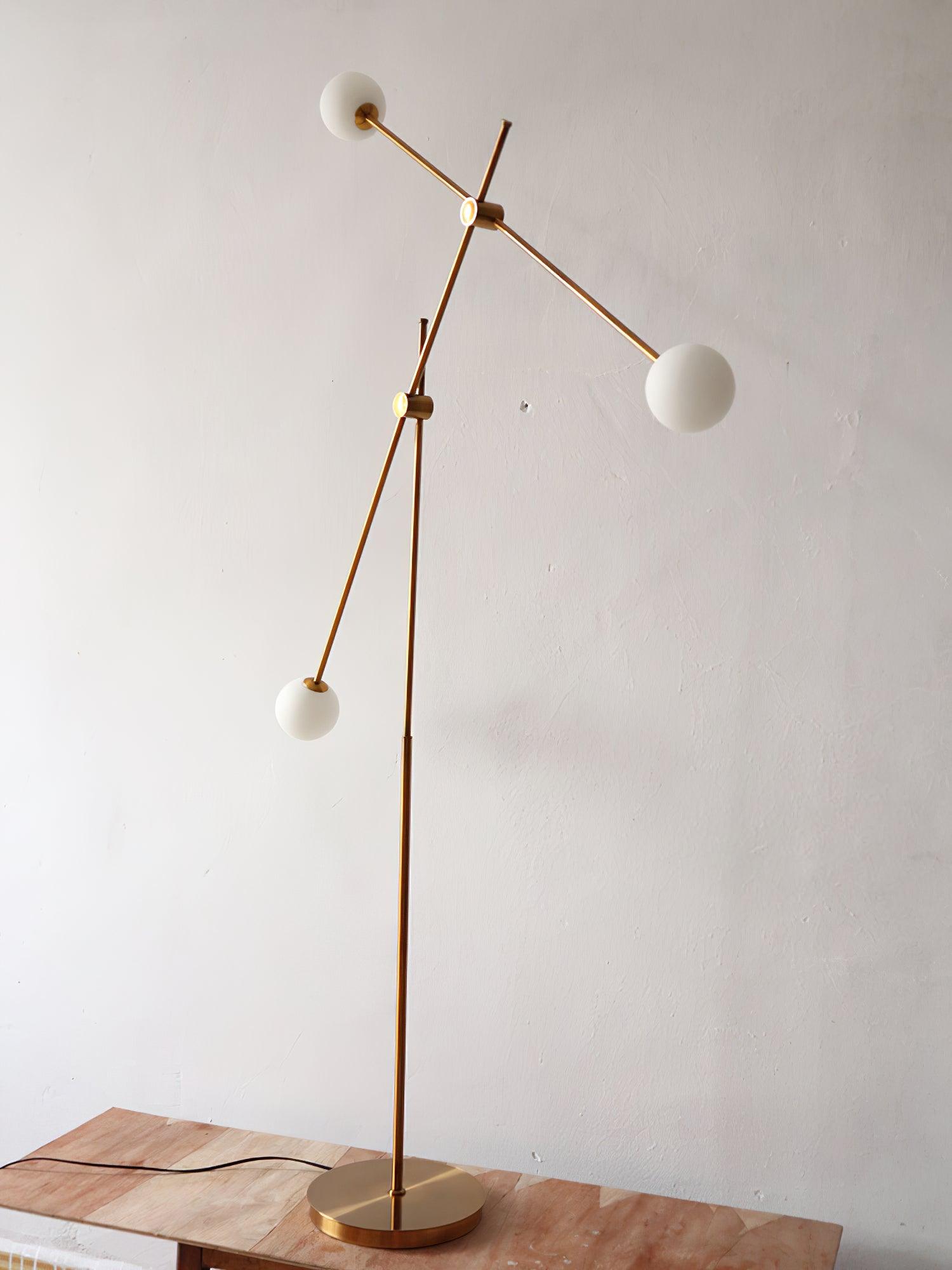 Unlit Kemi lamp on a wooden surface, with three white globes, a steep diagonal gold arm and a round gold base