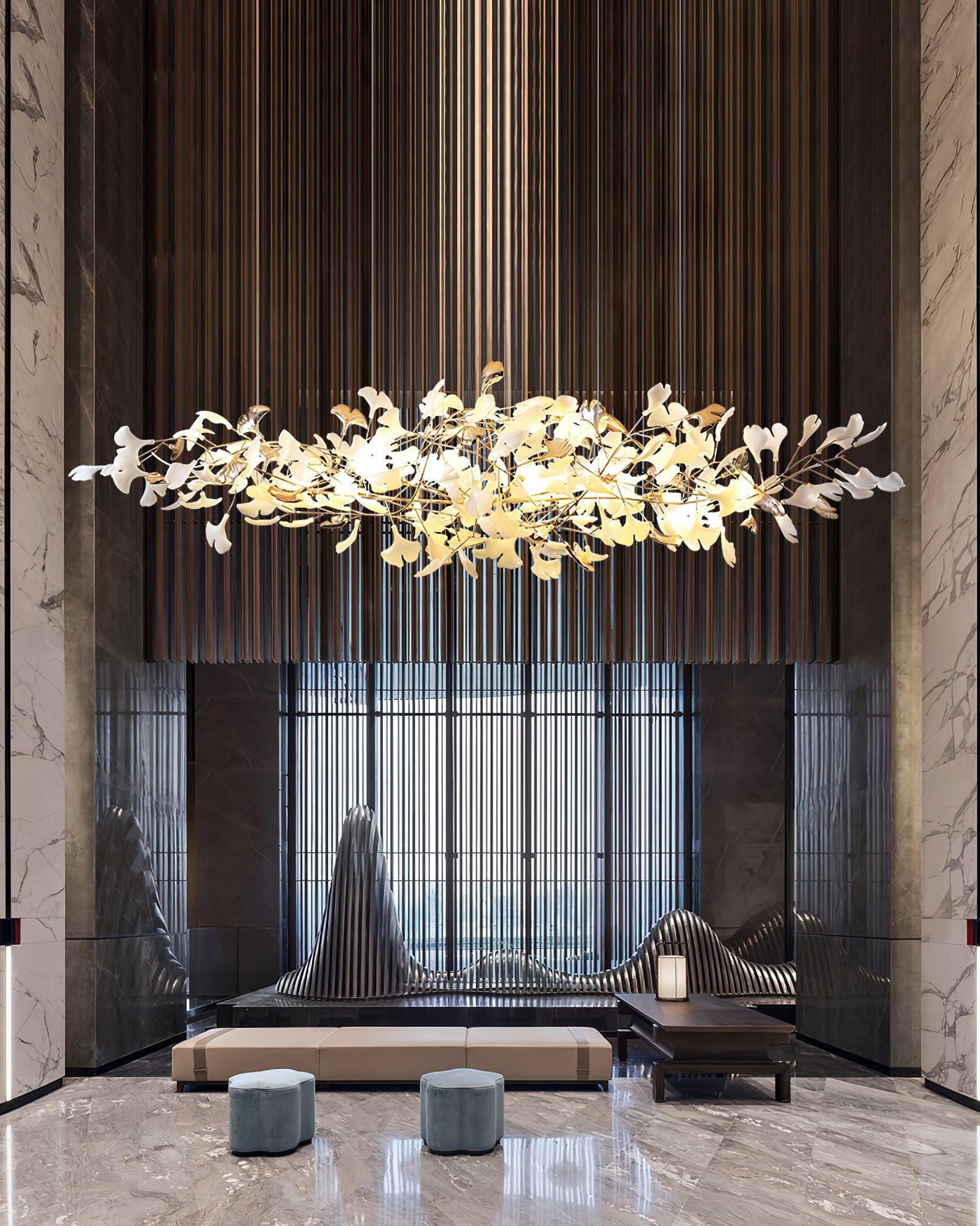 Portrait lounge view of white-and-gold leaf chandelier over pale bench and two blue stools between marble columns