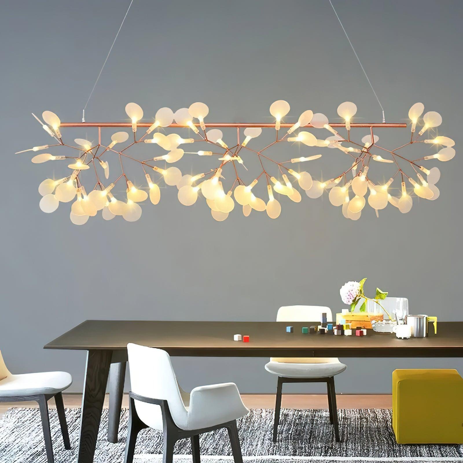 Rose-gold-colour branching petal chandelier above dark dining table with white chairs and small decorative objects