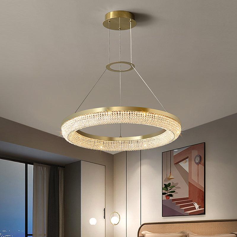 Single gold crystal ring chandelier above a bed, with separate small bedside lights in the background