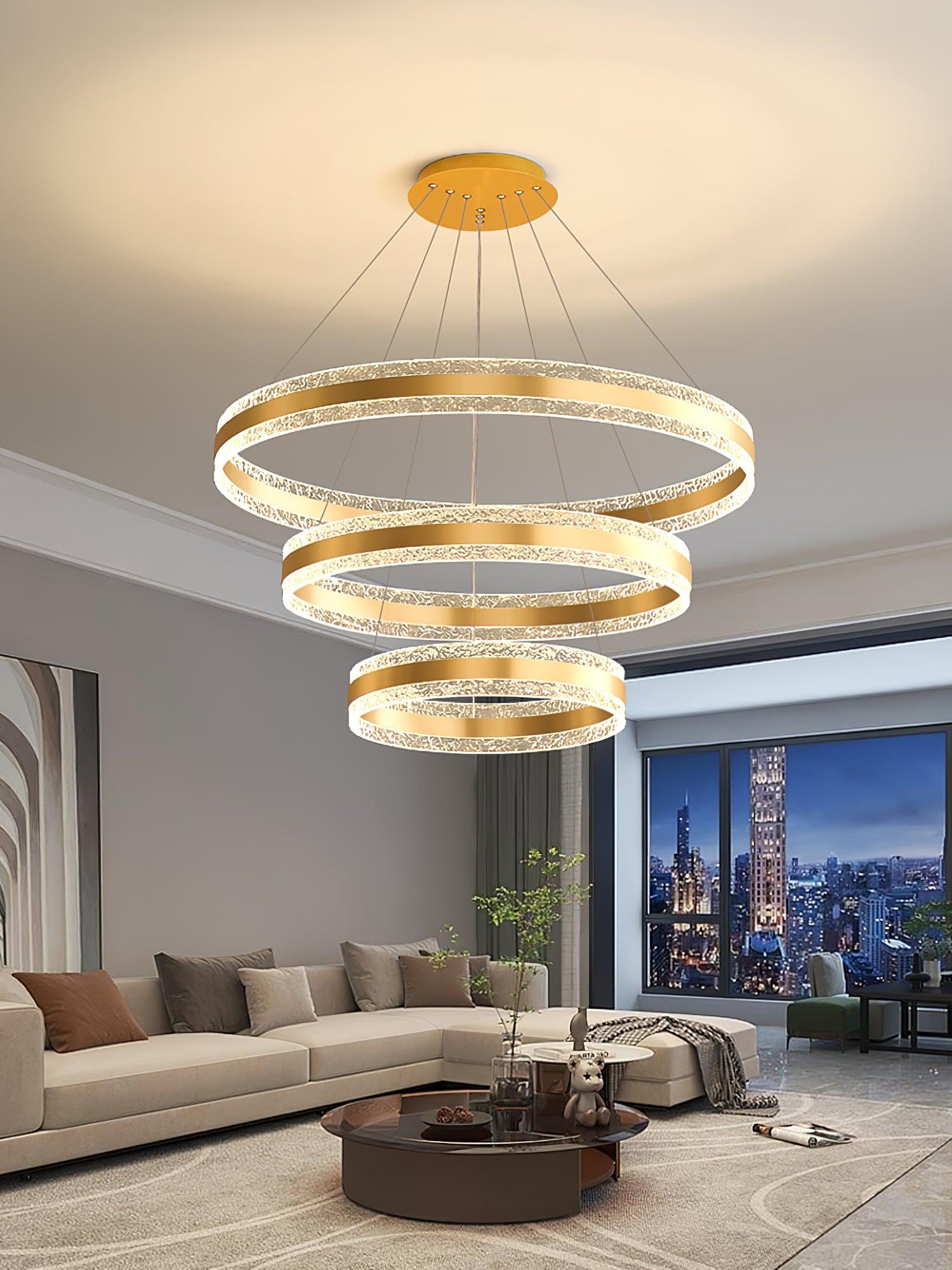 Three gold-tone LED rings above a grey sectional sofa beside a city-view window at night