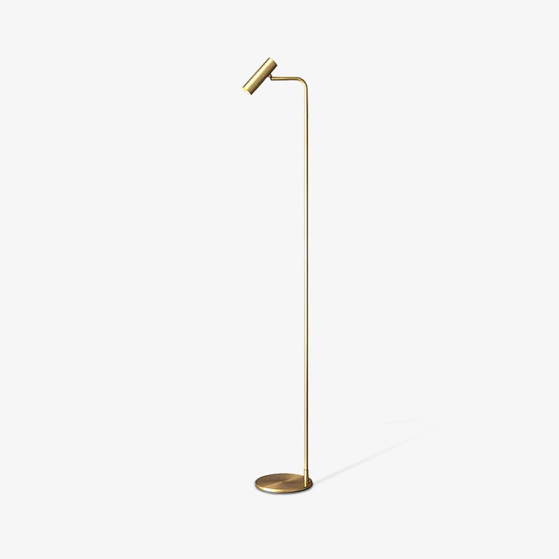 Small gold-coloured floor lamp with cylindrical head and circular base on a pale background with a long diagonal shadow