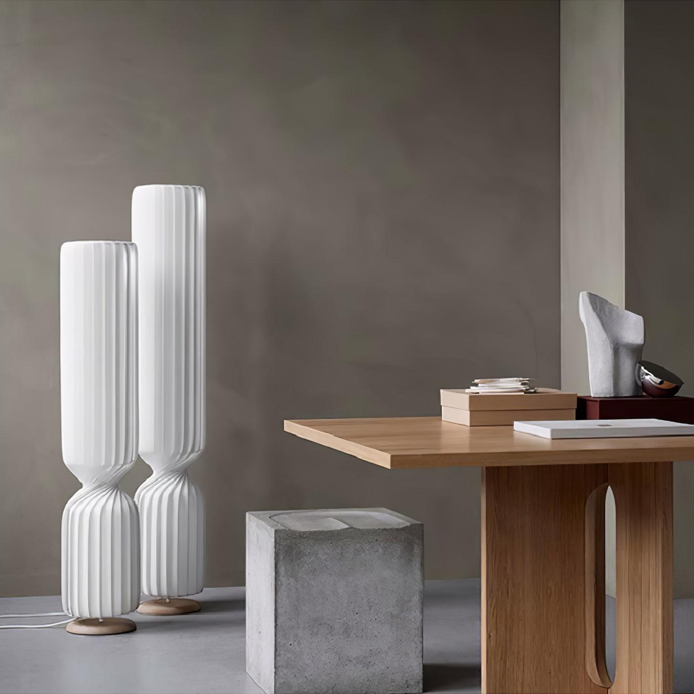 Two unlit-looking white twist lamps beside wooden console and gray block stool, pale round bases and white floor cords