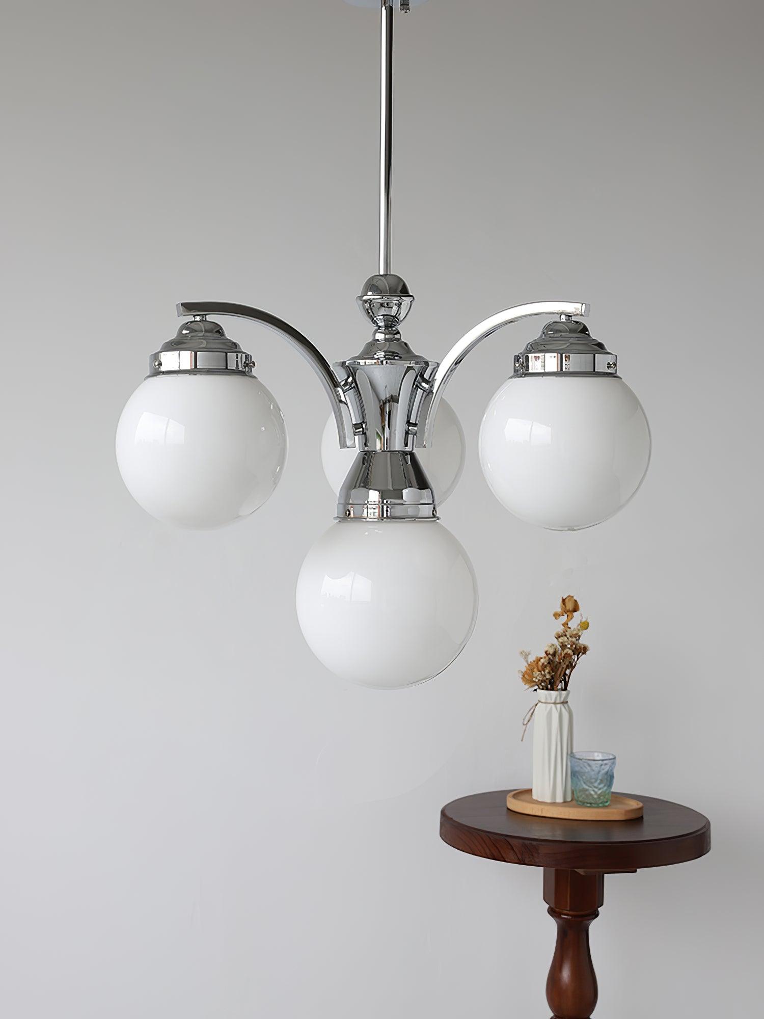 White globes hanging below curved chrome arms with a central lower globe above a wood side table and vase