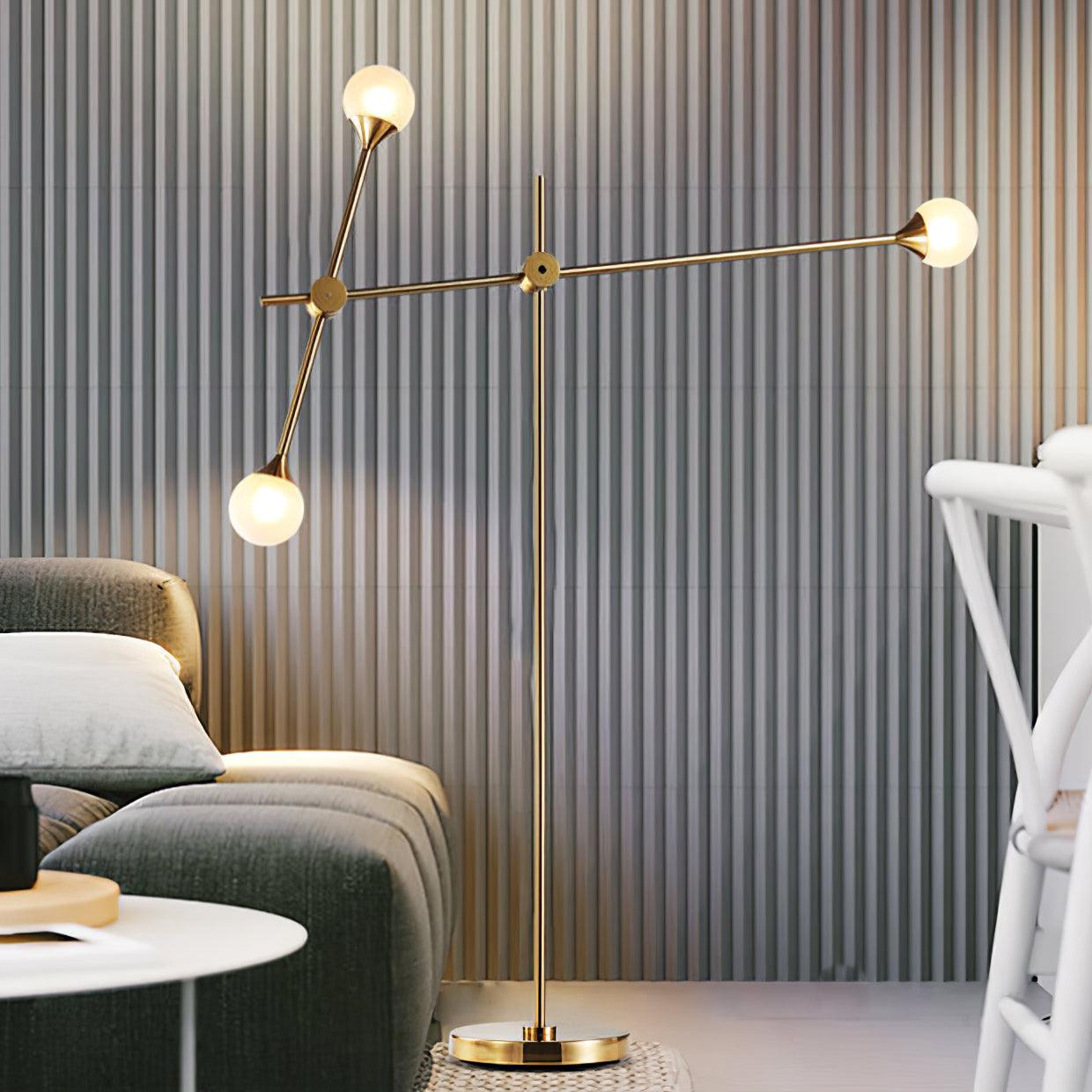 Kemi lamp glowing beside a grey sofa and ribbed wall, with a nearly horizontal gold arm and three round shades