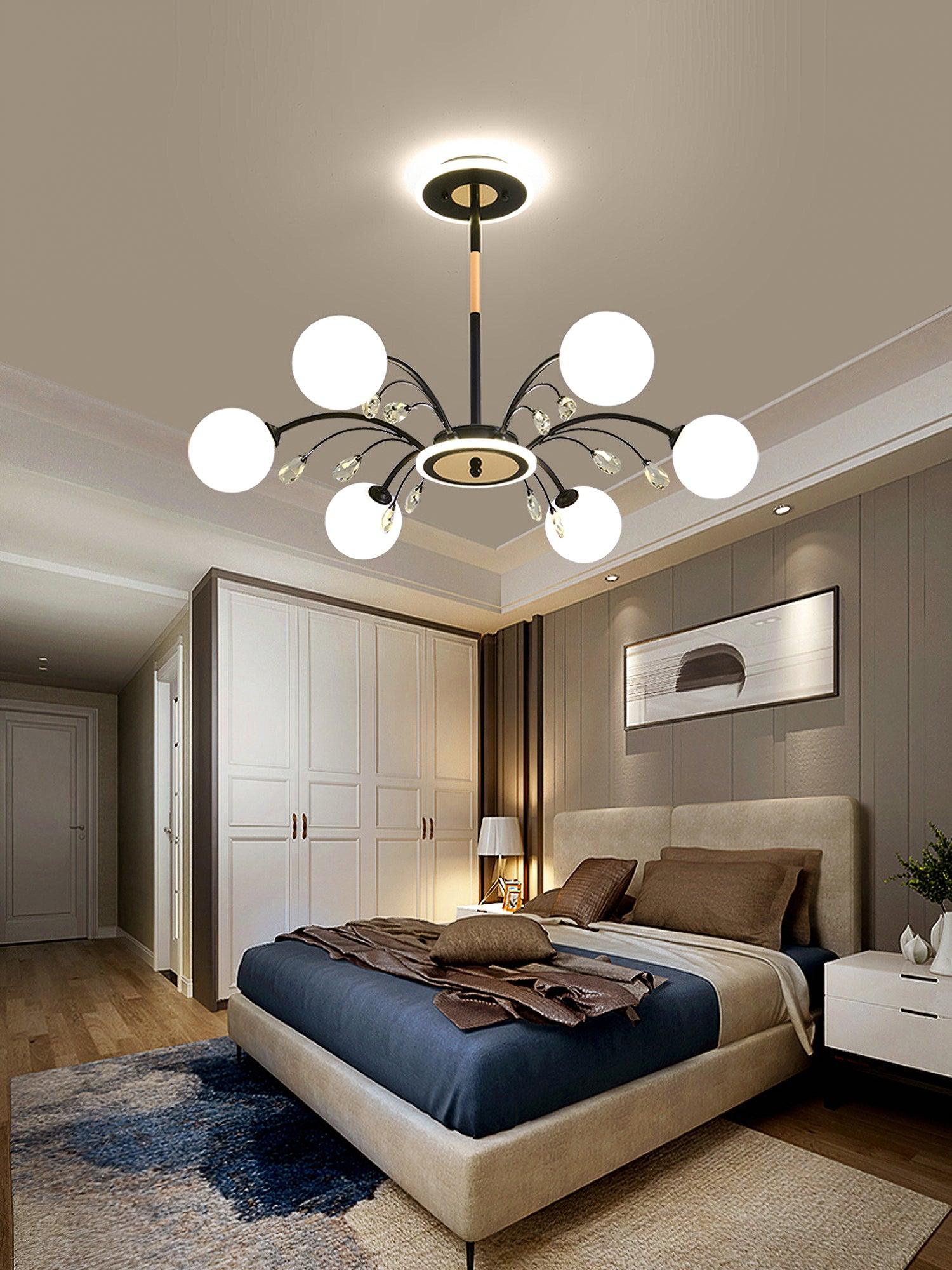 Black six-globe chandelier over upholstered bed and brown bedding, with white wardrobe, bedside lamp and grey wall portrait