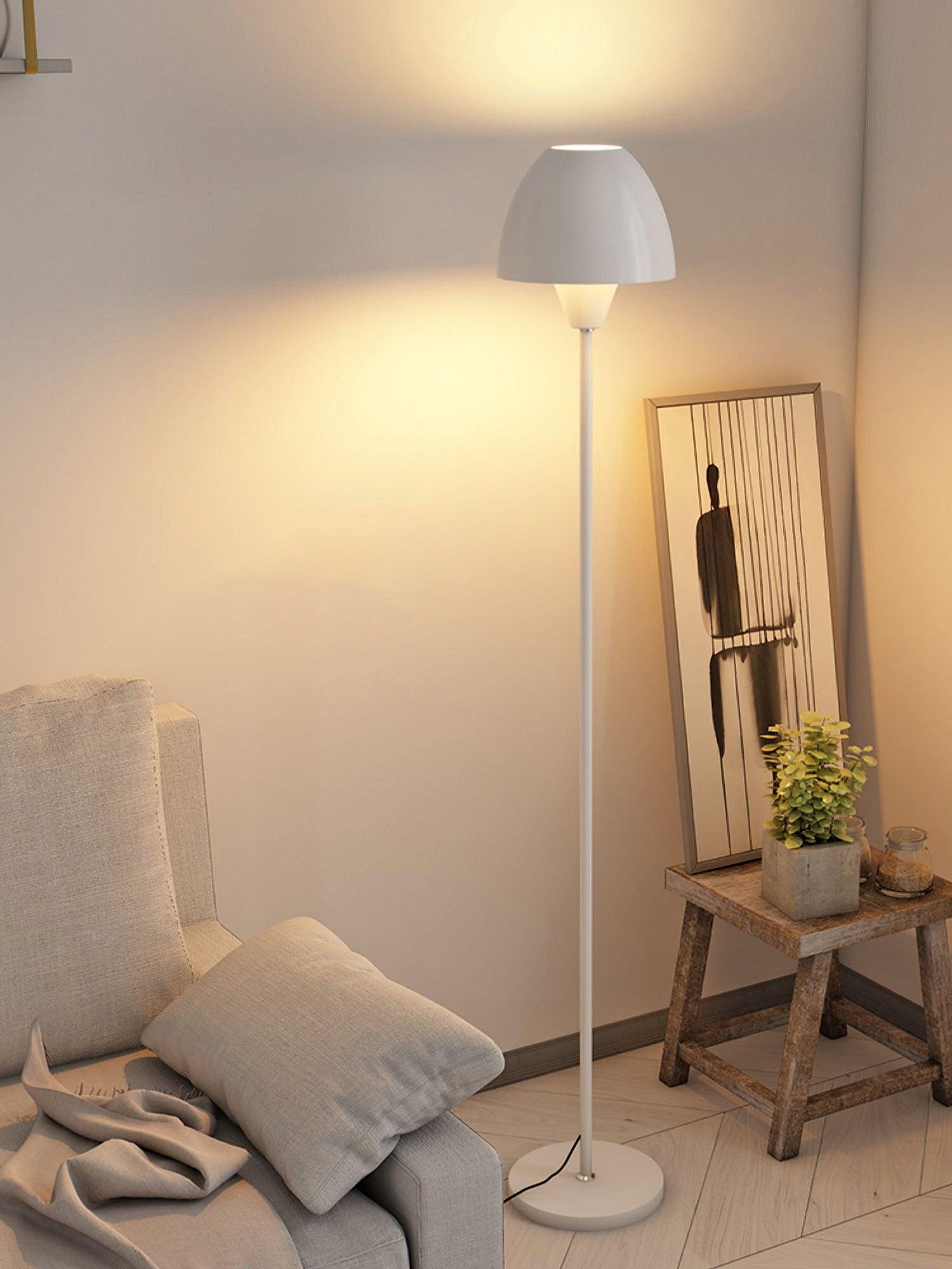 White floor lamp beside a pale seat and wooden stool holding a framed print and a potted plant
