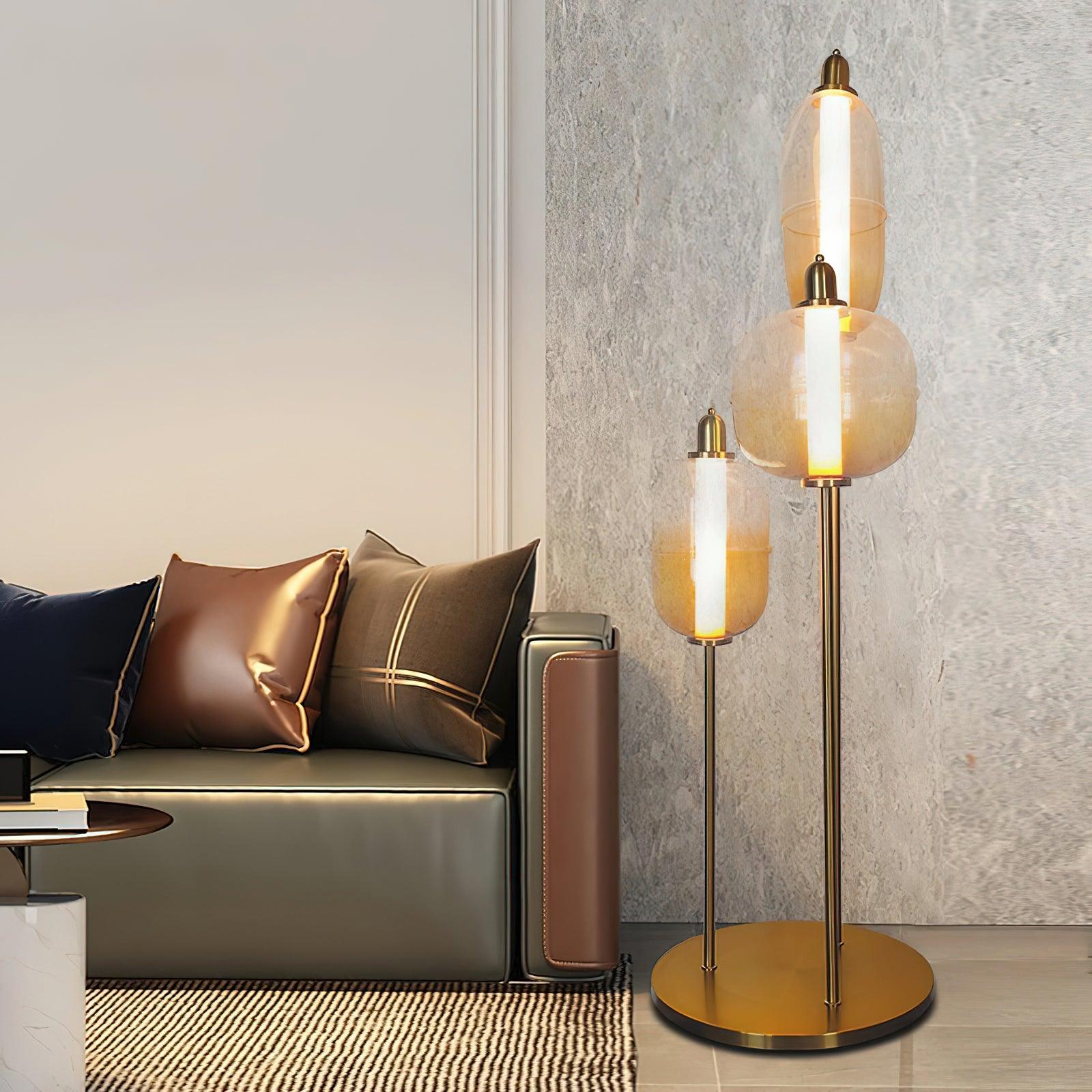Three glowing amber glass shades on gold stems beside a green sofa with bronze and navy cushions and a striped rug