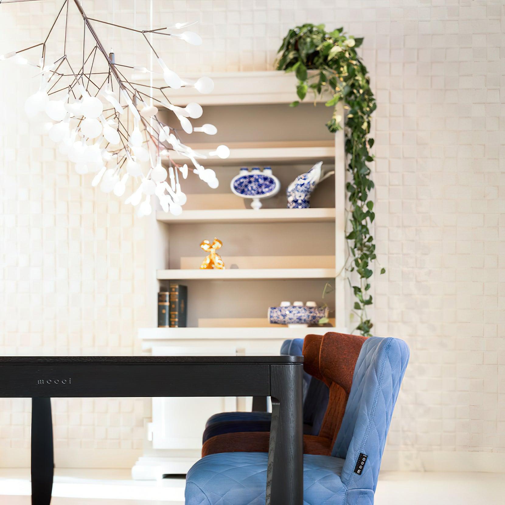 Oblique end view of petal chandelier over black table and blue and rust chairs, with ceramics and trailing plant on shelves