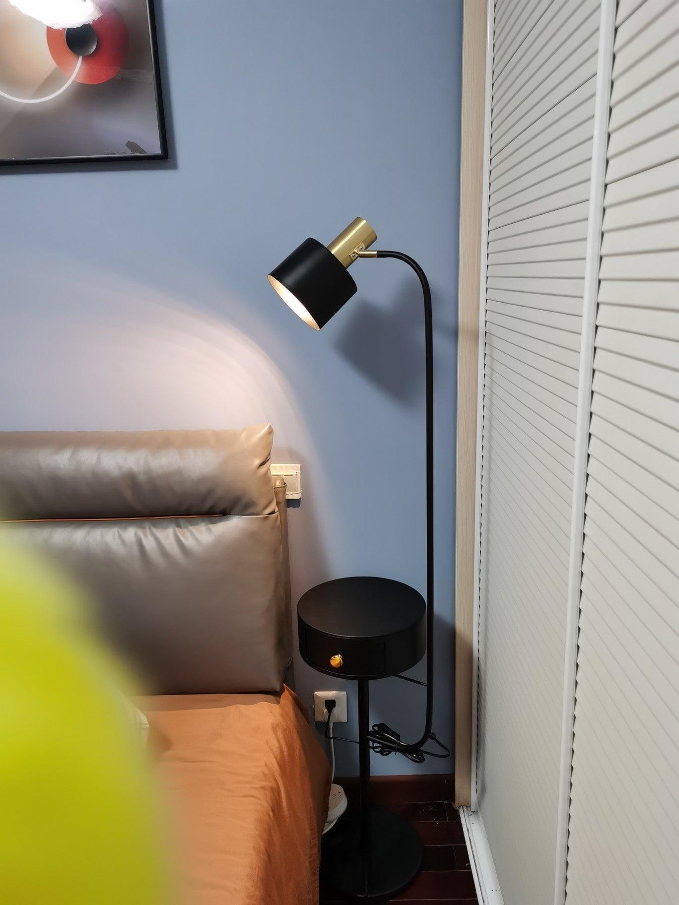Black lamp lit beside upholstered bed and white closet doors, gold fitting, black round closed drawer table and coiled cord