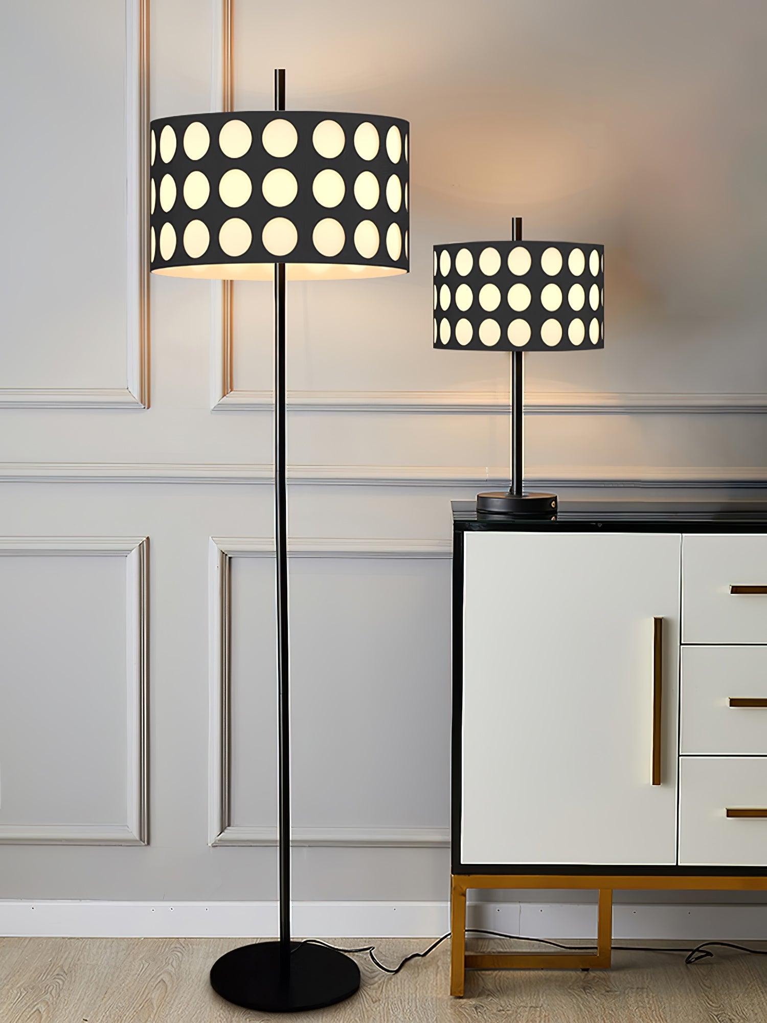 Straight black floor lamp and smaller dotted-shade table lamp beside cabinet and abstract artwork, floor cord visible
