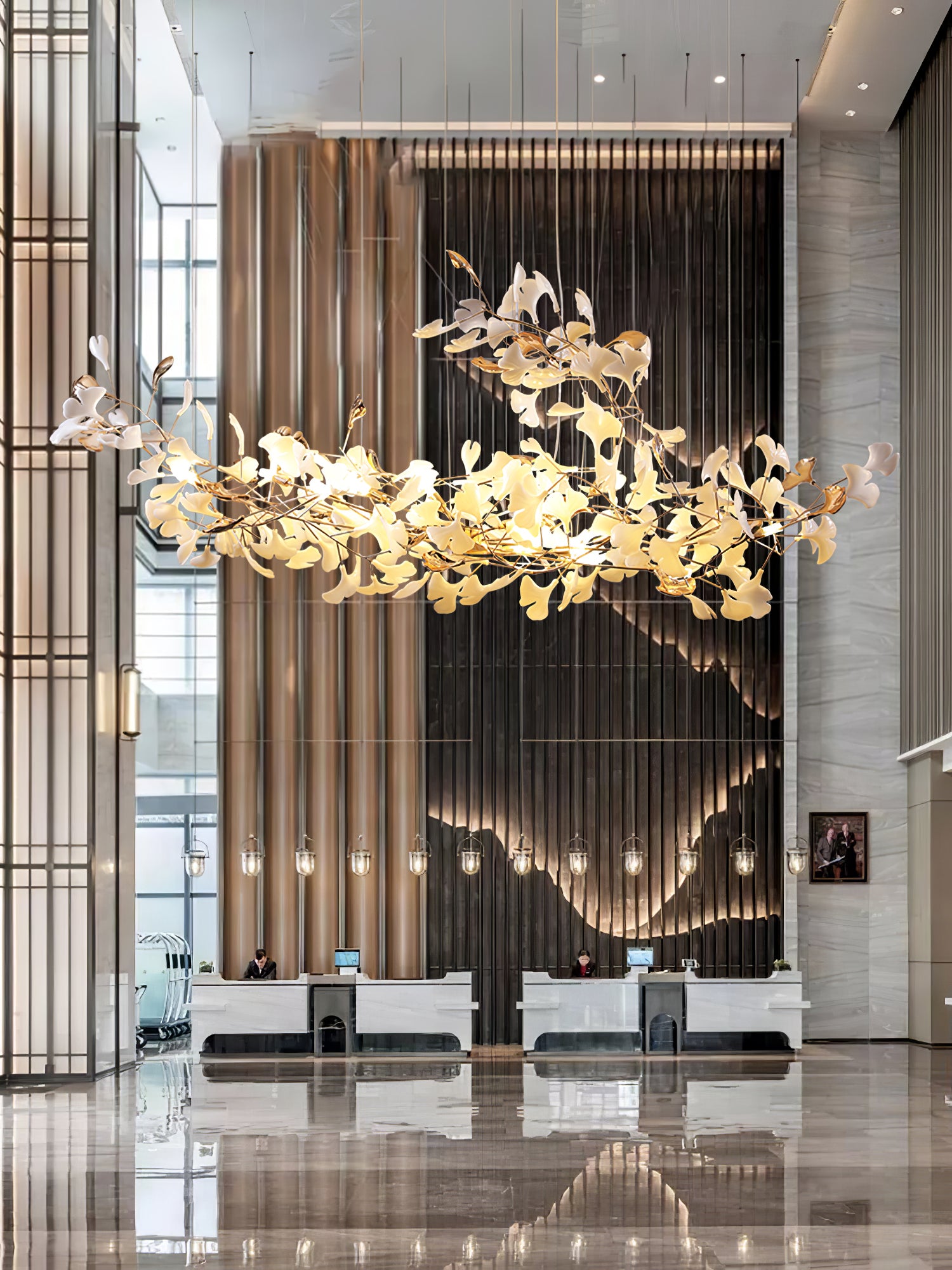 Portrait tall reception view with raised-sweep leaf chandelier, gold-toned column and marble desk reflected below
