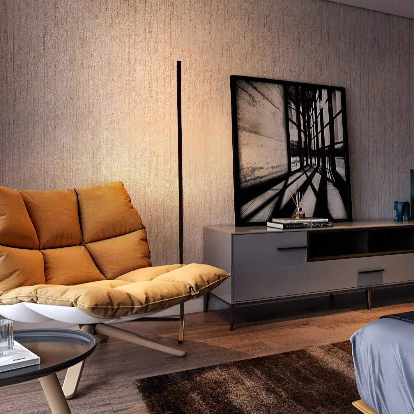 Slim black lamp lighting the wall beside a mustard chair, sideboard and large monochrome artwork
