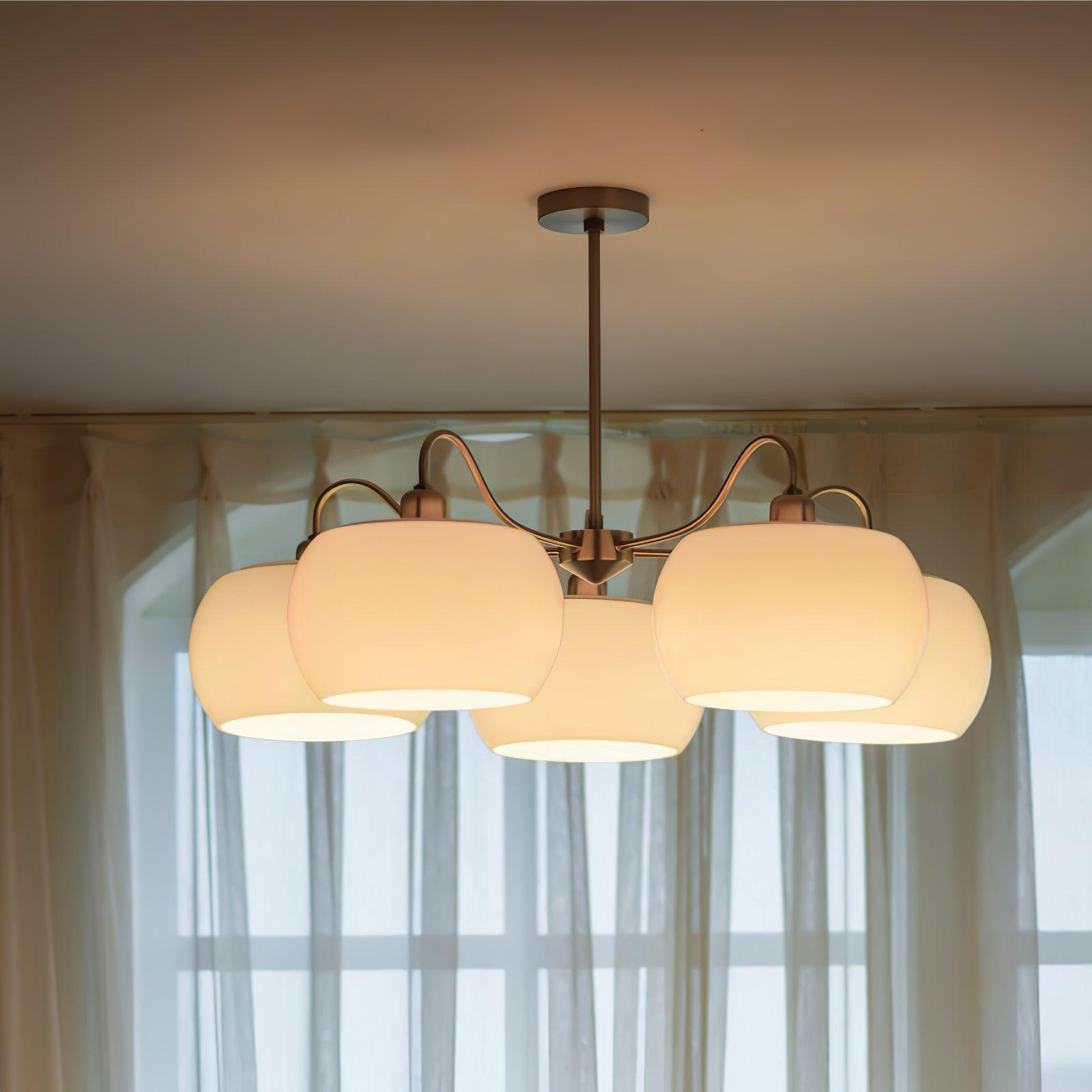 Illuminated five-light white glass chandelier with curved nickel-tone arms near curtains