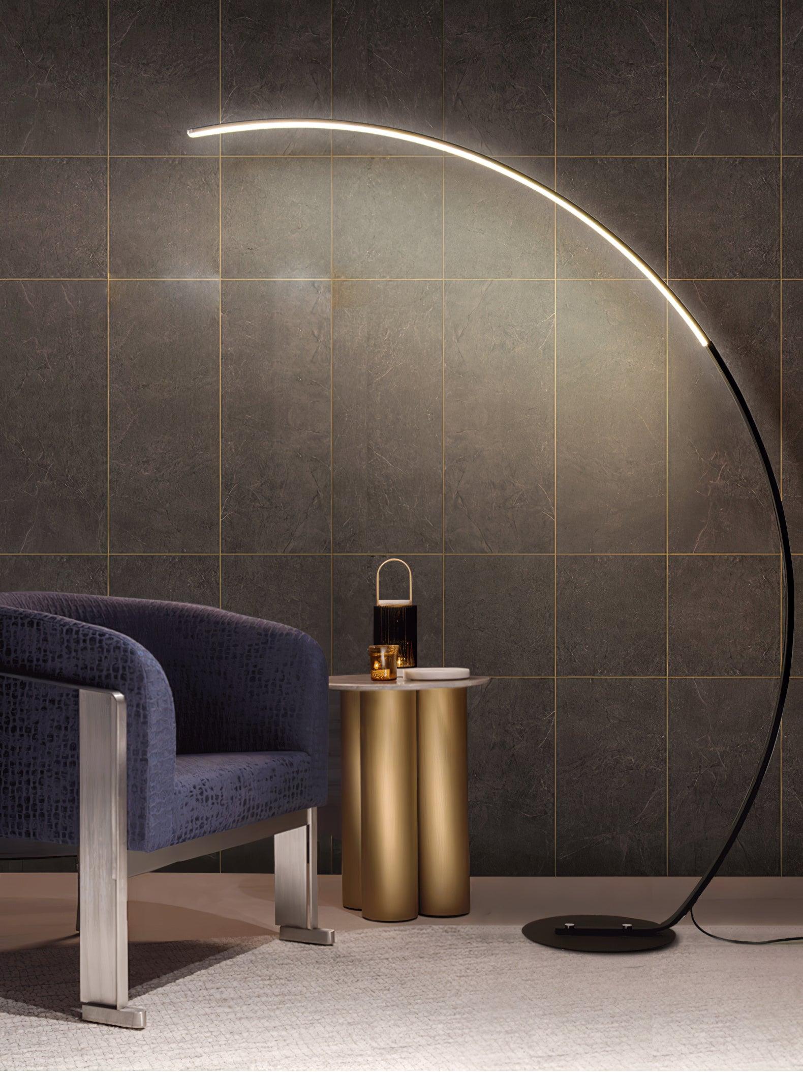 Black Arc floor lamp beside blue chair and gold-column side table, against dark stone wall with grid lines
